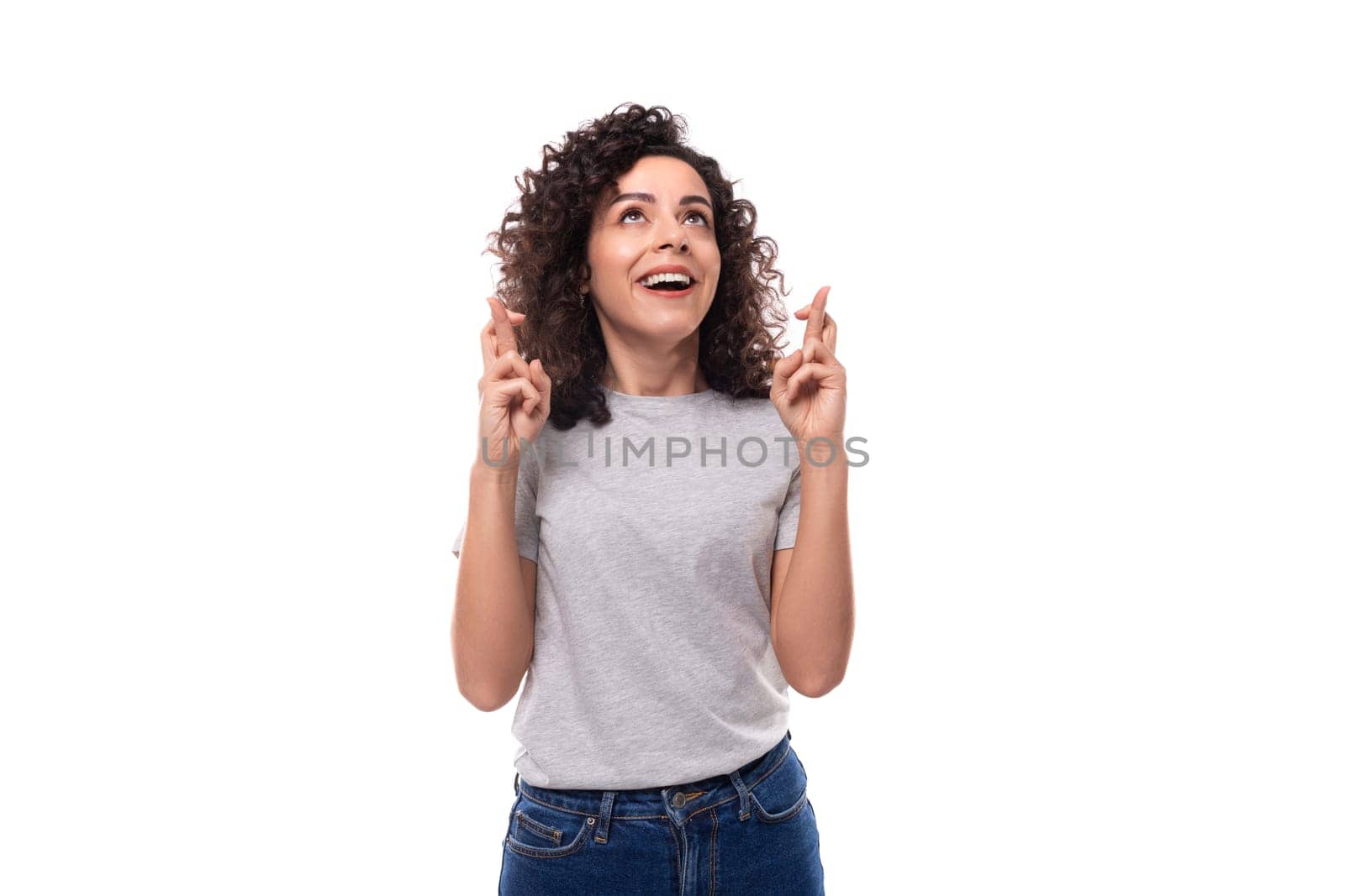 surprised european woman with black curly hair in a gray basic t-shirt points her fingers towards advertising space.