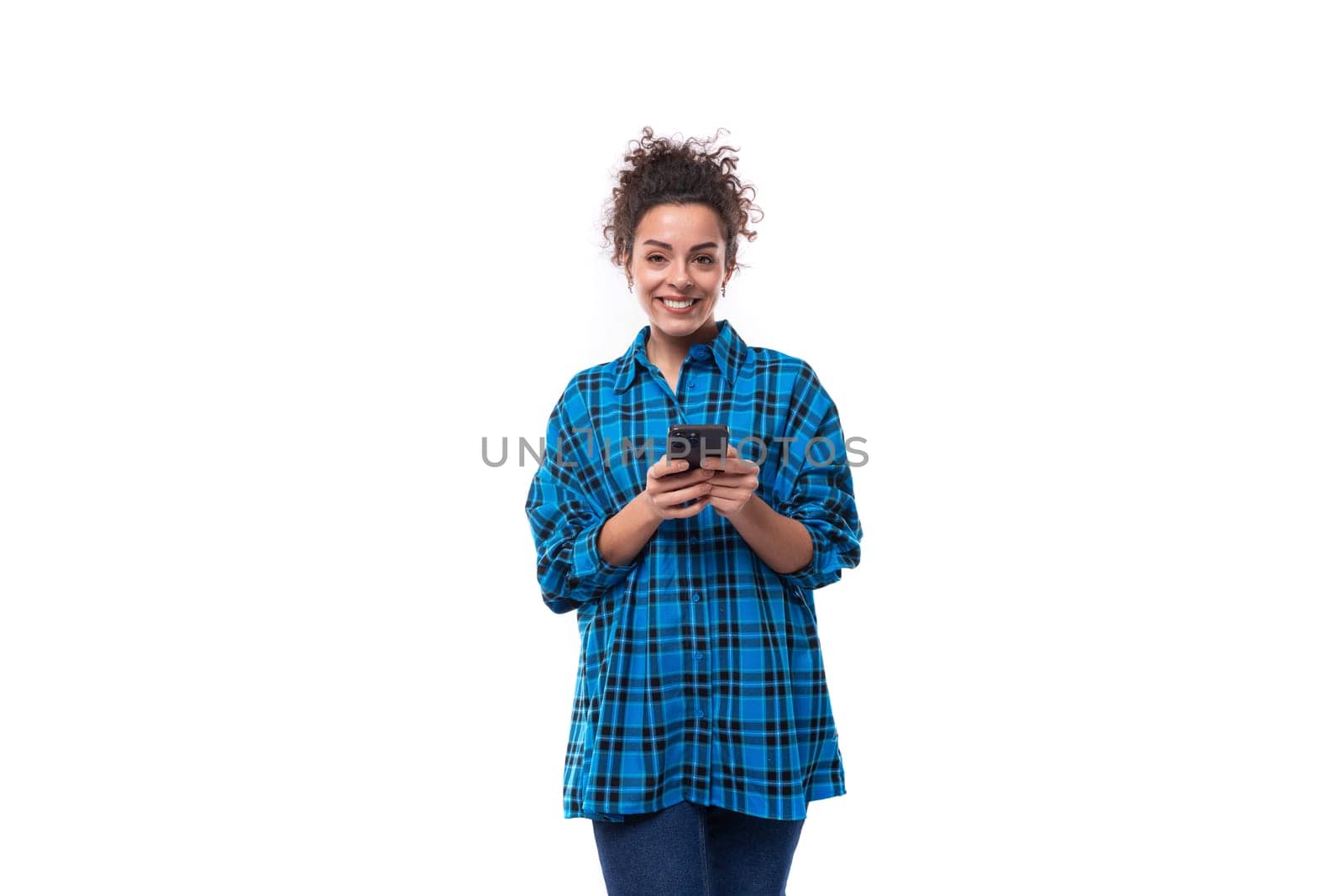 young beautiful european woman with curly hair dressed in a blue plaid shirt is chatting on the phone by TRMK
