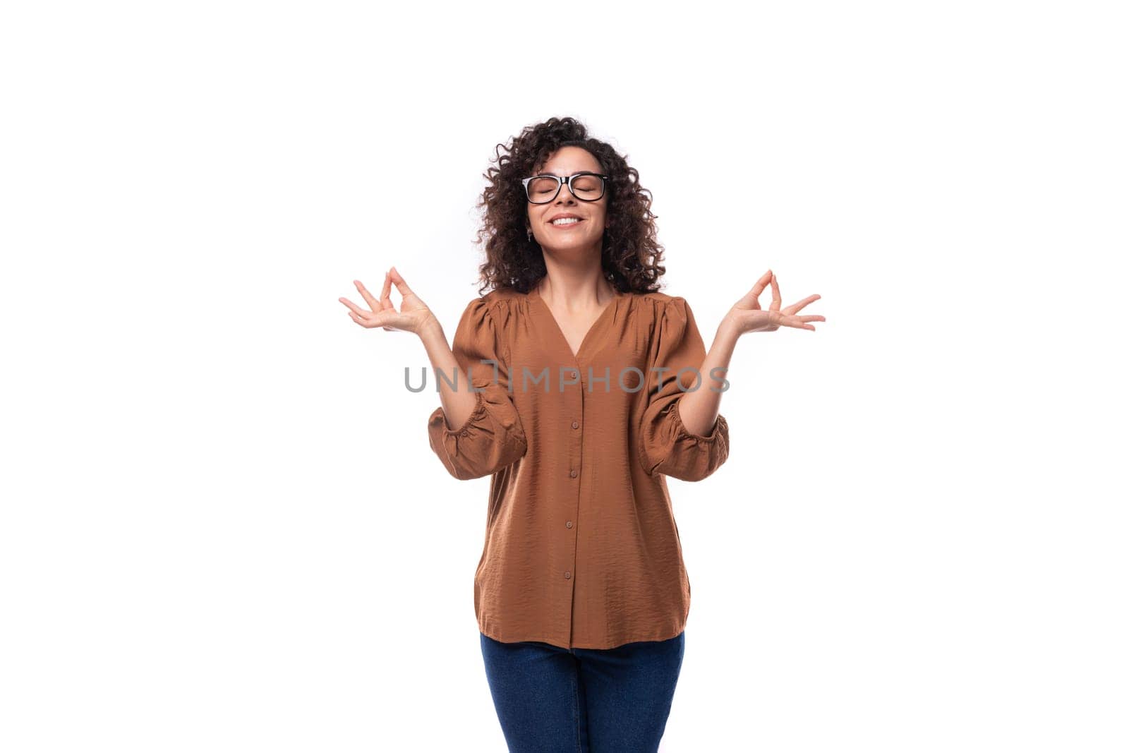 young positive cheerful slender woman with curls dressed in a brown blouse meditates.