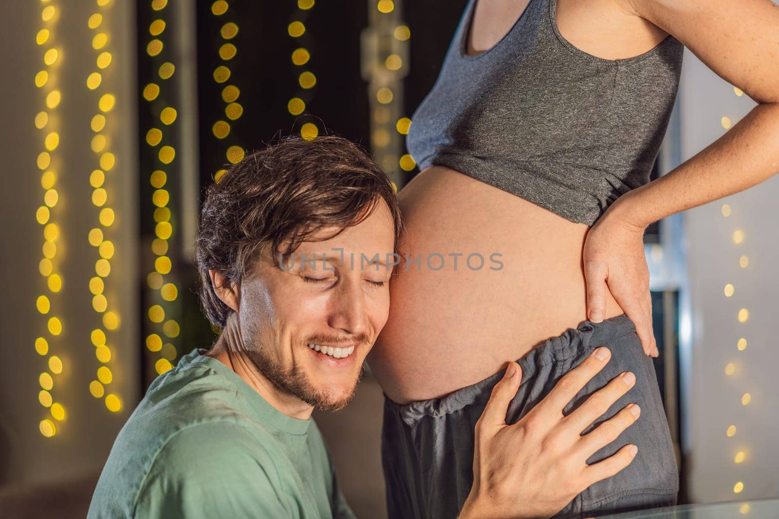 In a tender holiday moment, a husband kisses his wife's pregnant belly, expressing love and anticipation for the Christmas joy to come.