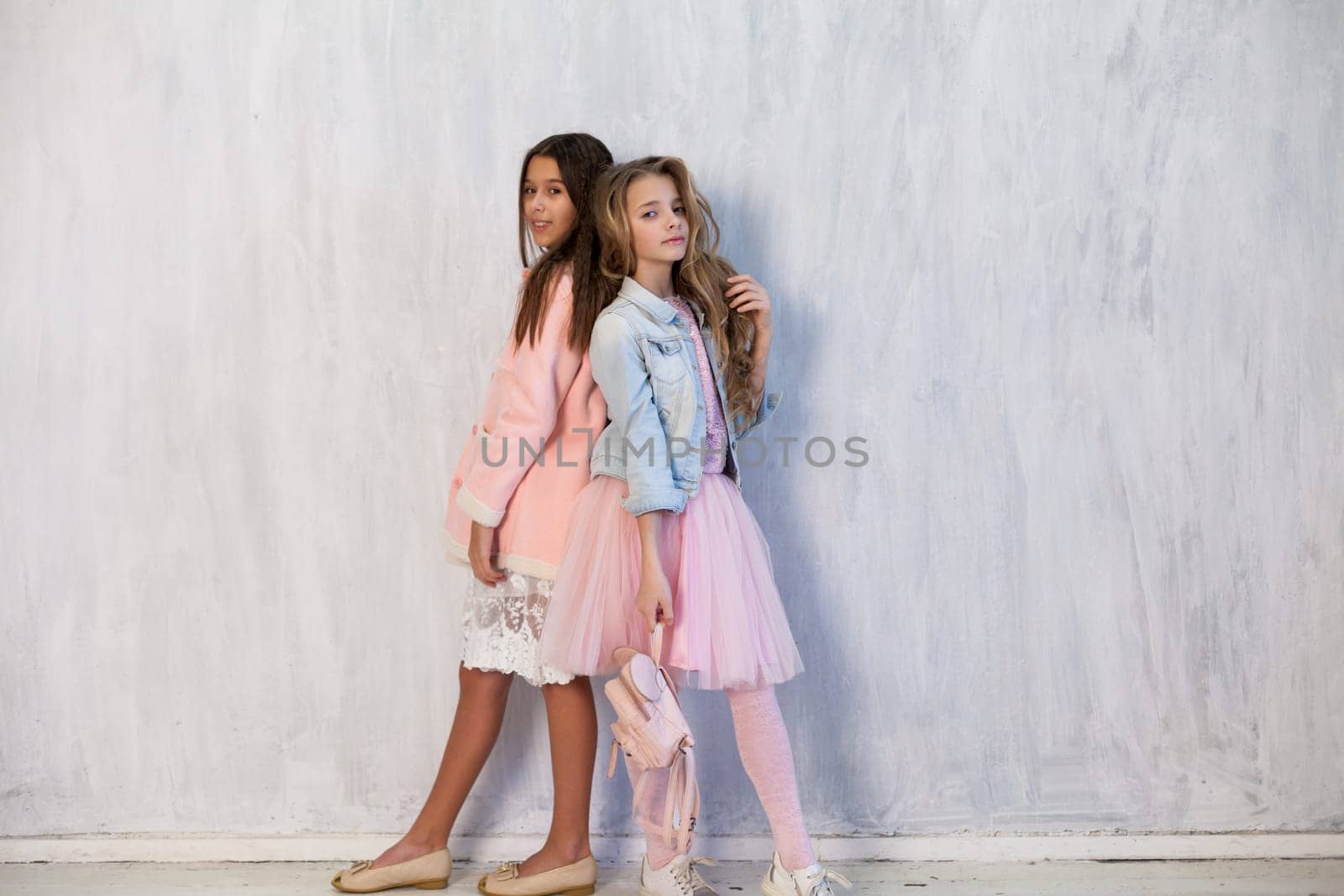 Portrait of two fashionable schoolgirl girls girlfriend in pink clothes on a grey background