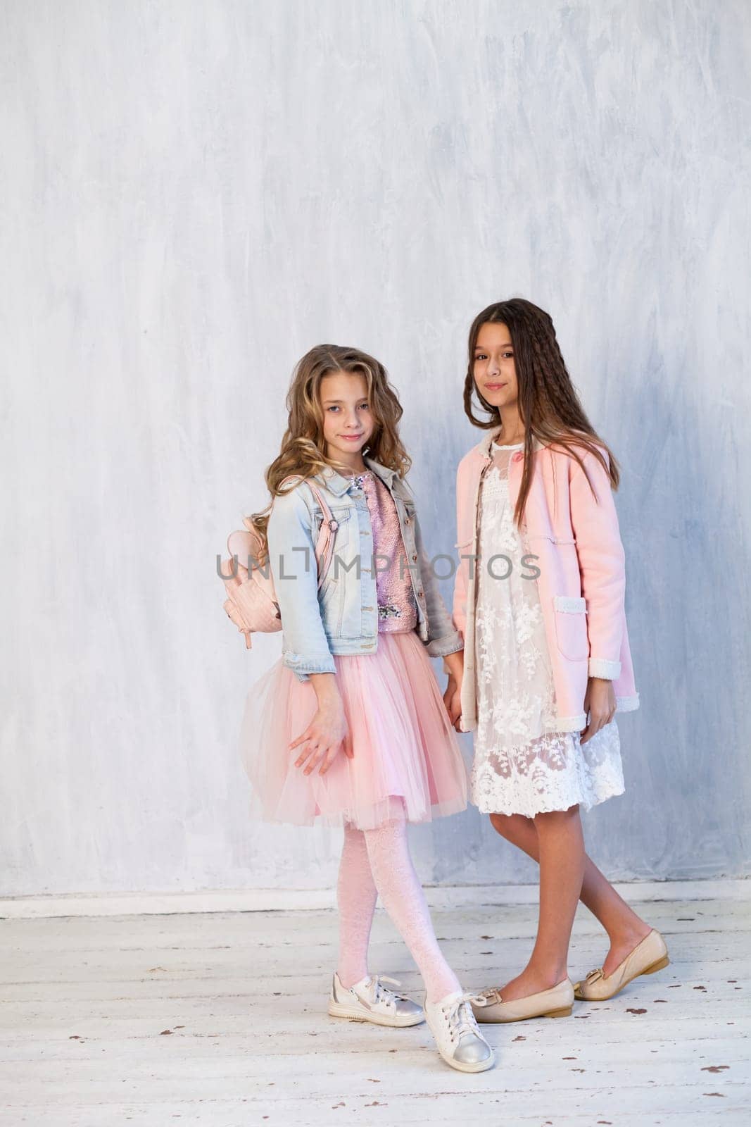 Portrait of two fashionable schoolgirl girls girlfriend in pink clothes on a grey background