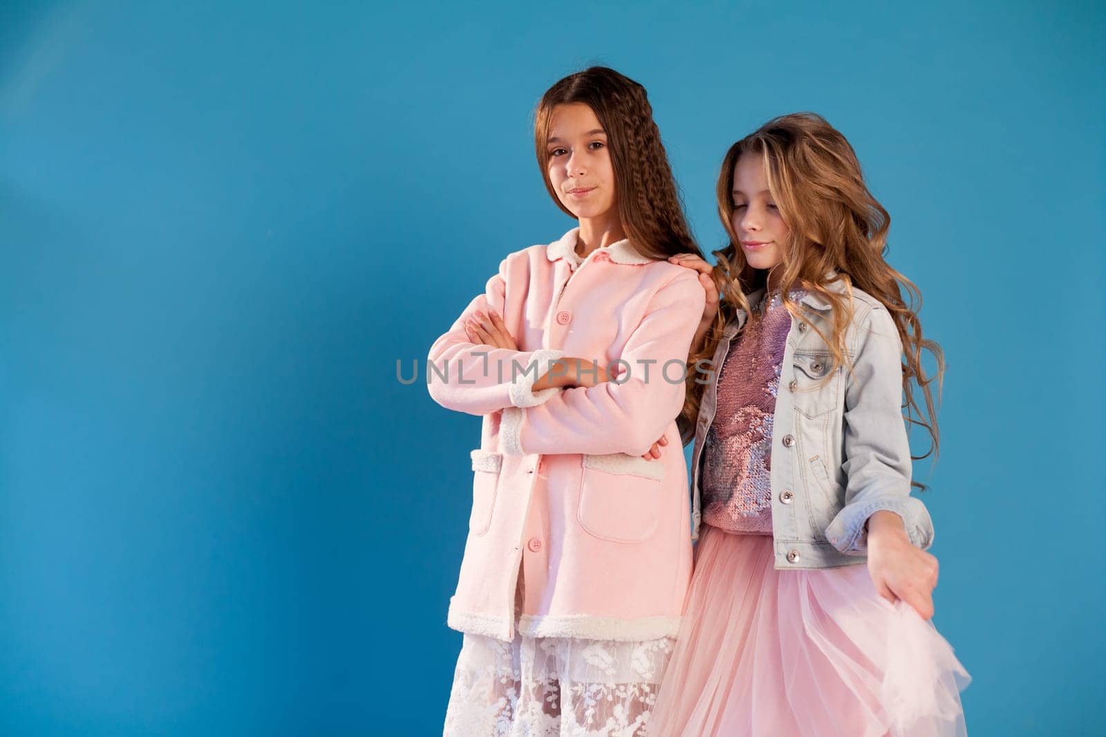 Portrait of two fashionable schoolgirl girls girlfriend in pink clothes on a blue background