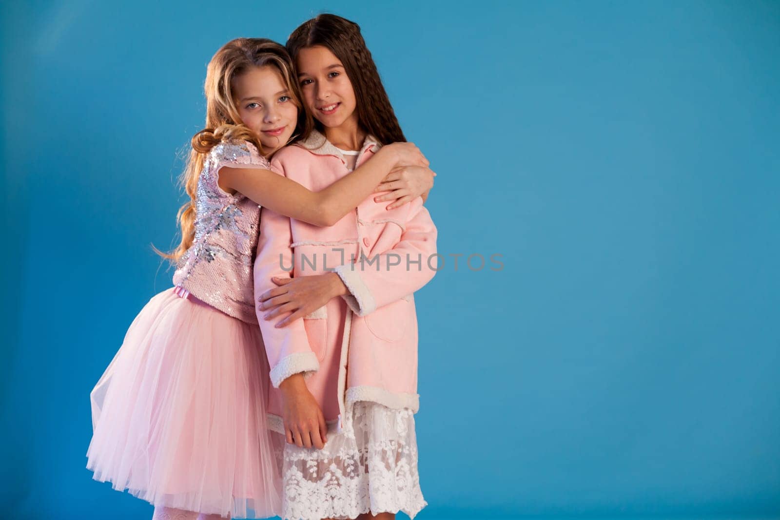 Portrait of two fashionable schoolgirl girls girlfriend in pink clothes on a blue background