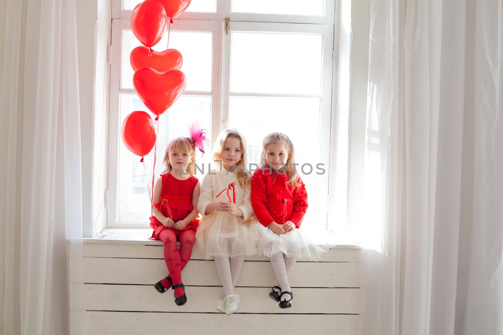 three little girls in red and white dresses sitting by the window by Simakov