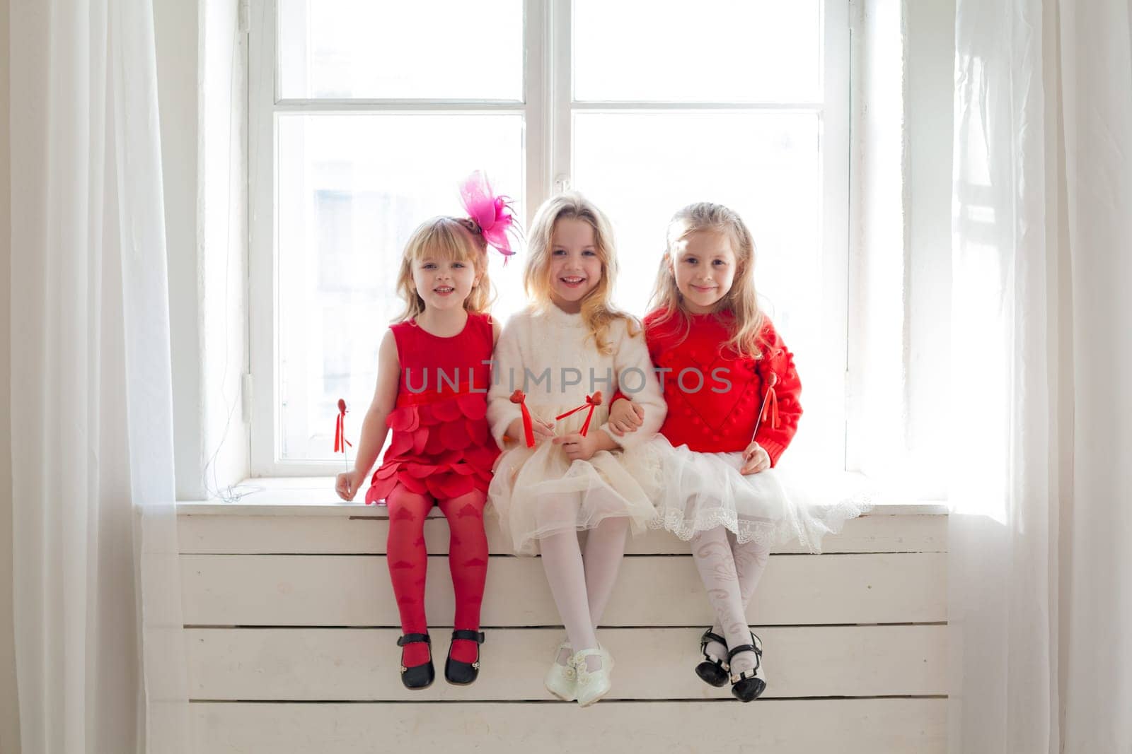 three little girls in red and white dresses sitting by the window by Simakov