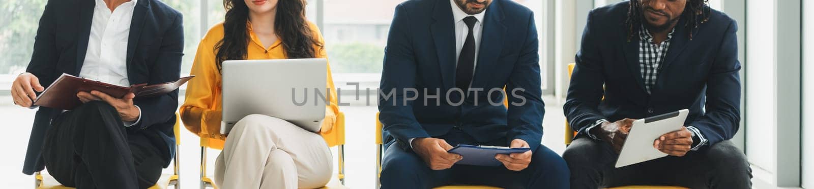 Diversity candidates siting while waiting for job interview in front view. Low section crop of interviewees sitting on a chair while preparing their document and holding their laptop. Intellectual.