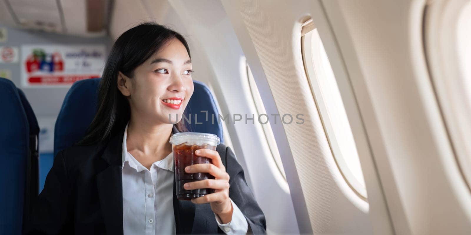 Successful Asian business woman, Business woman working in airplane on laptop computer and looking out the window.