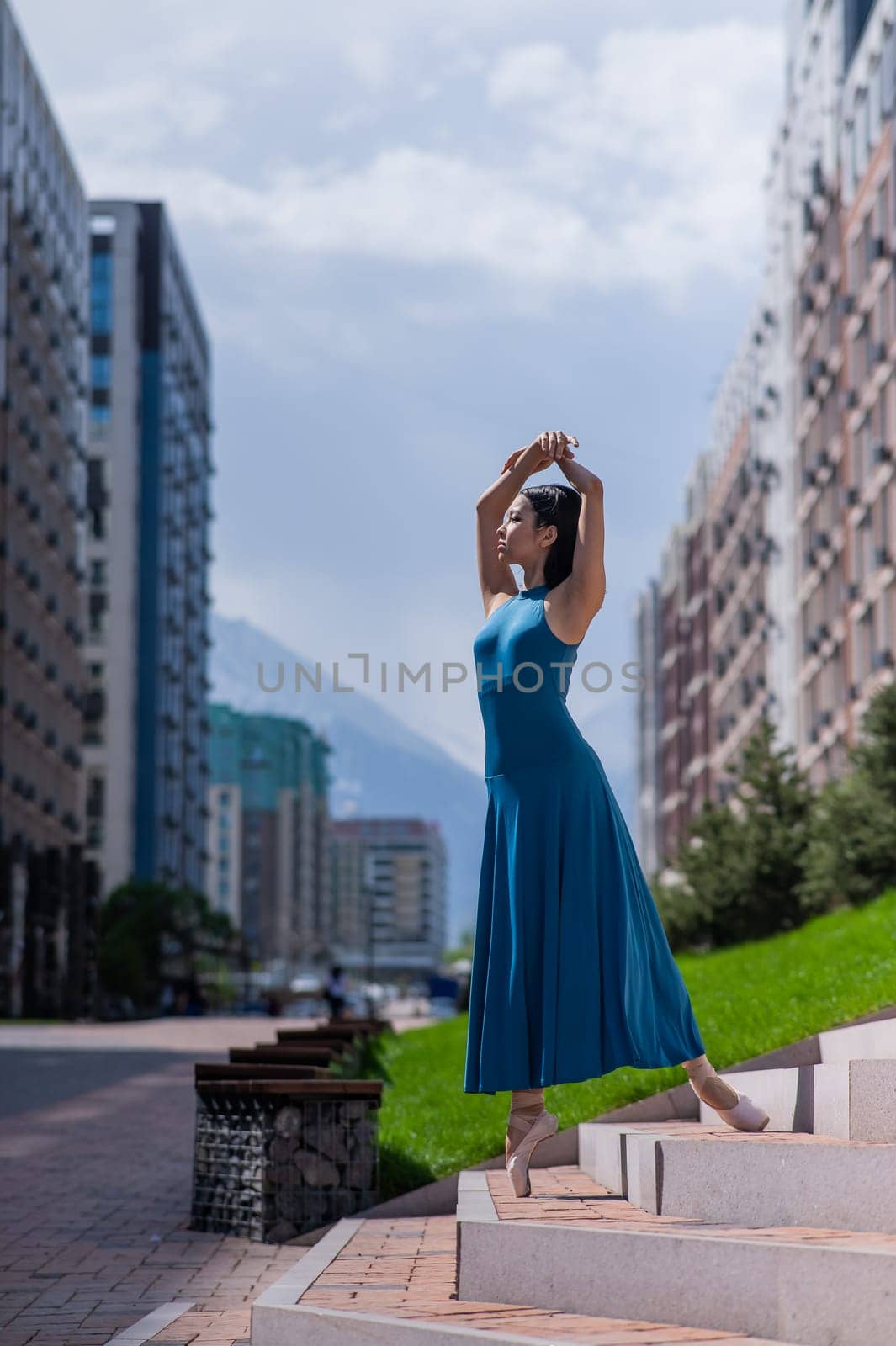 Beautiful Asian ballerina in blue dress posing on stairs outdoors. Urban landscape. Vertical photo