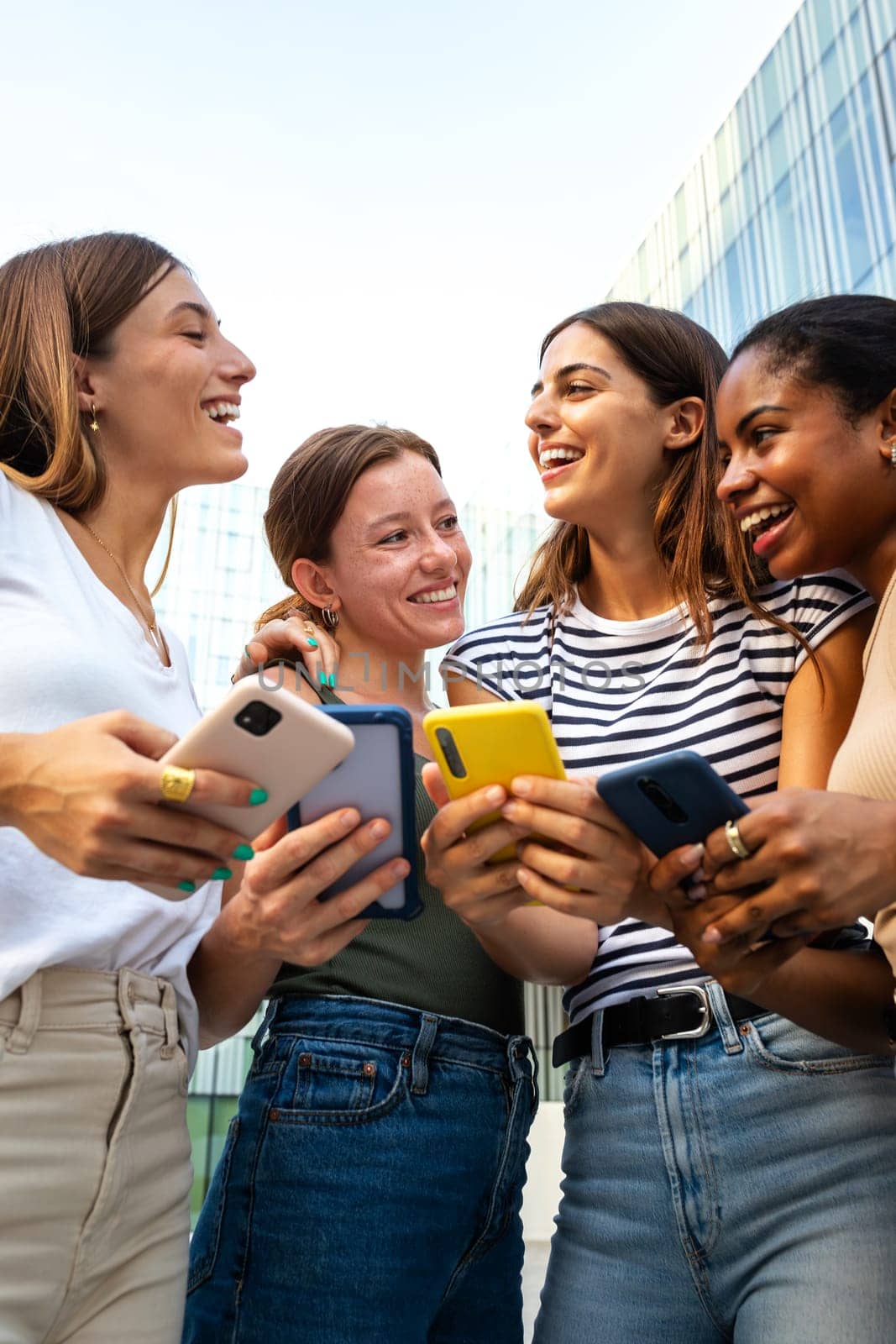 Vertical portrait of happy multiracial group of young women friends laughing and having fun while using mobile phones. by Hoverstock