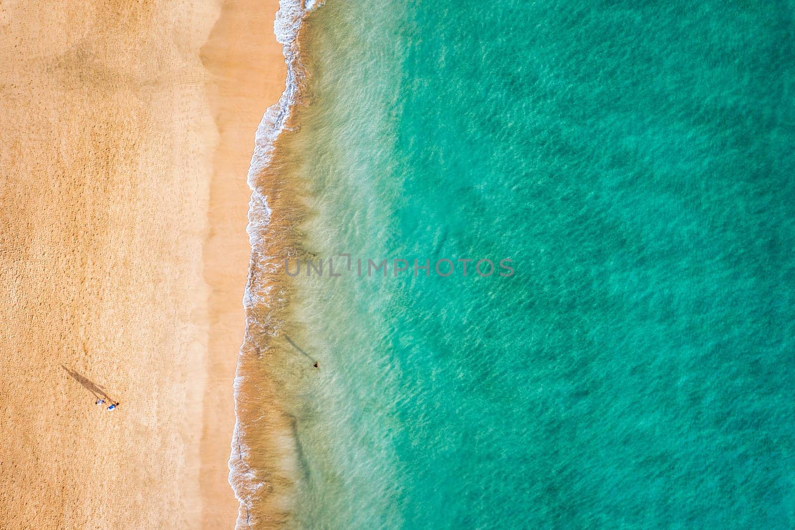 Aerial view of the walking people on the white sandy beach near sea with waves at sunset. Summer holiday. Top view of sporty people, clear azure water. Lifestyle and sport