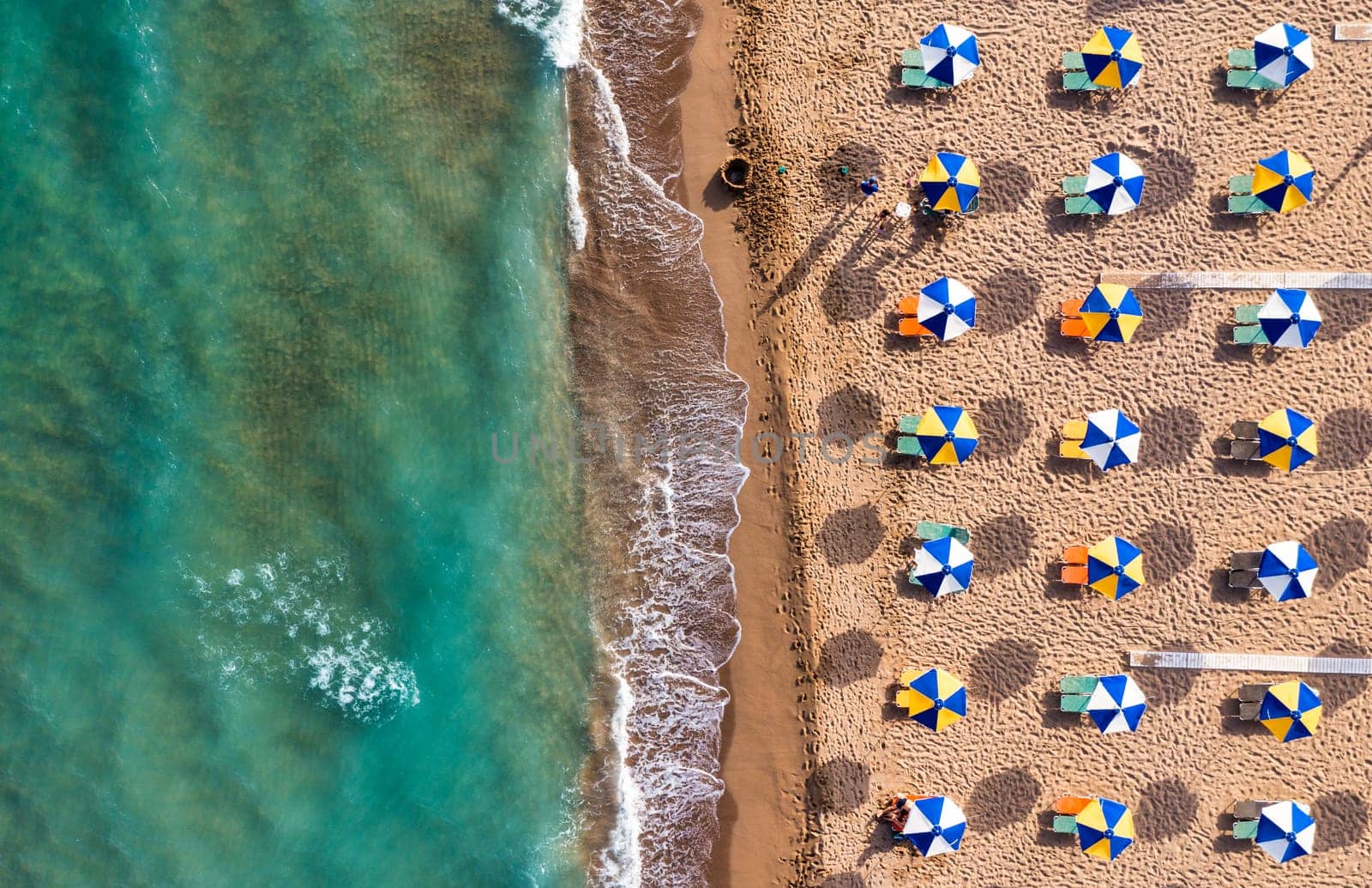 Concept of summer vacation. View from above, stunning aerial view of an amazing beach with beach umbrellas and turquoise clear water. Top view on a sun lounger under an umbrella on the sandy beach