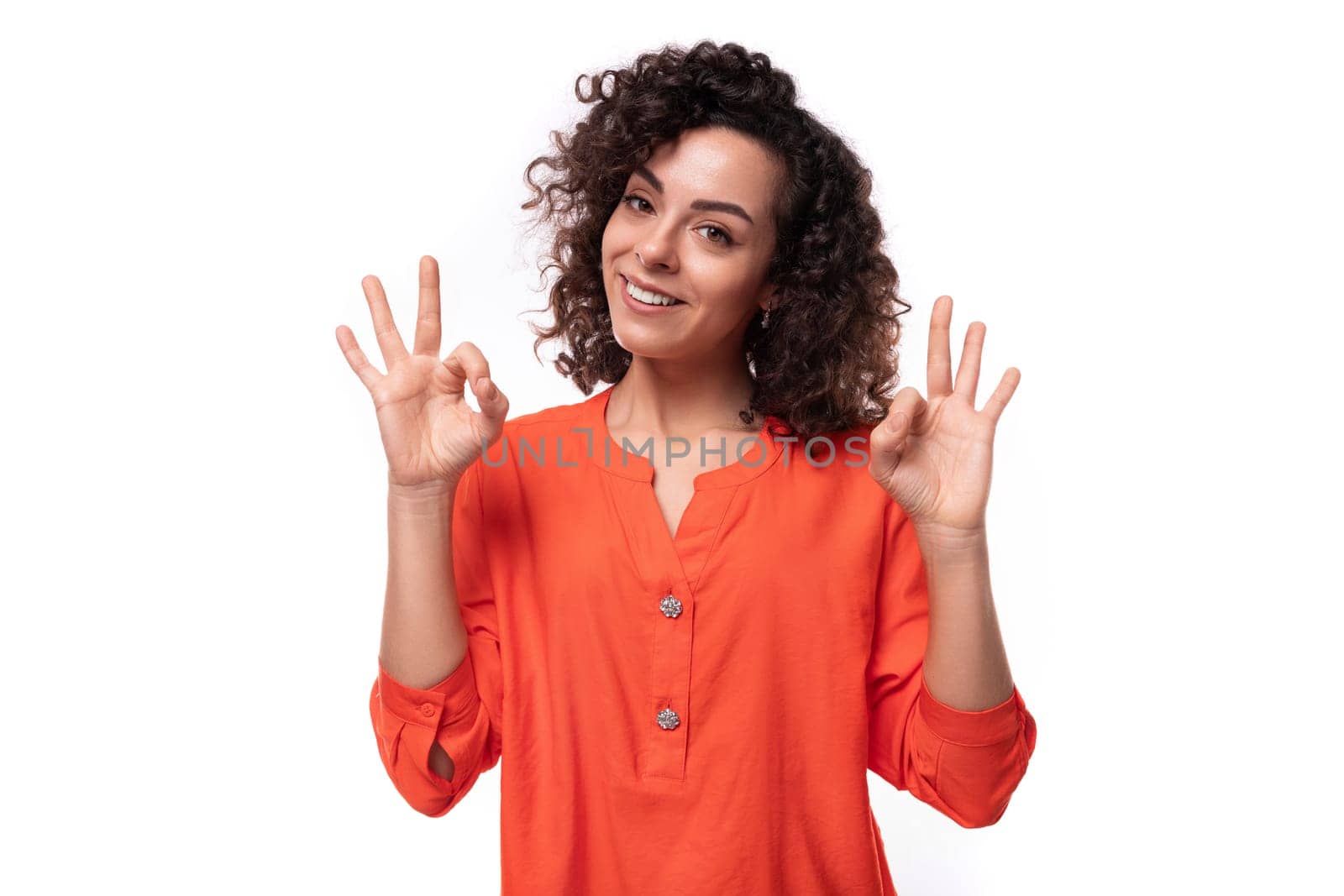 young successful european woman with curly black hair keeps dressed in a bright orange blouse.