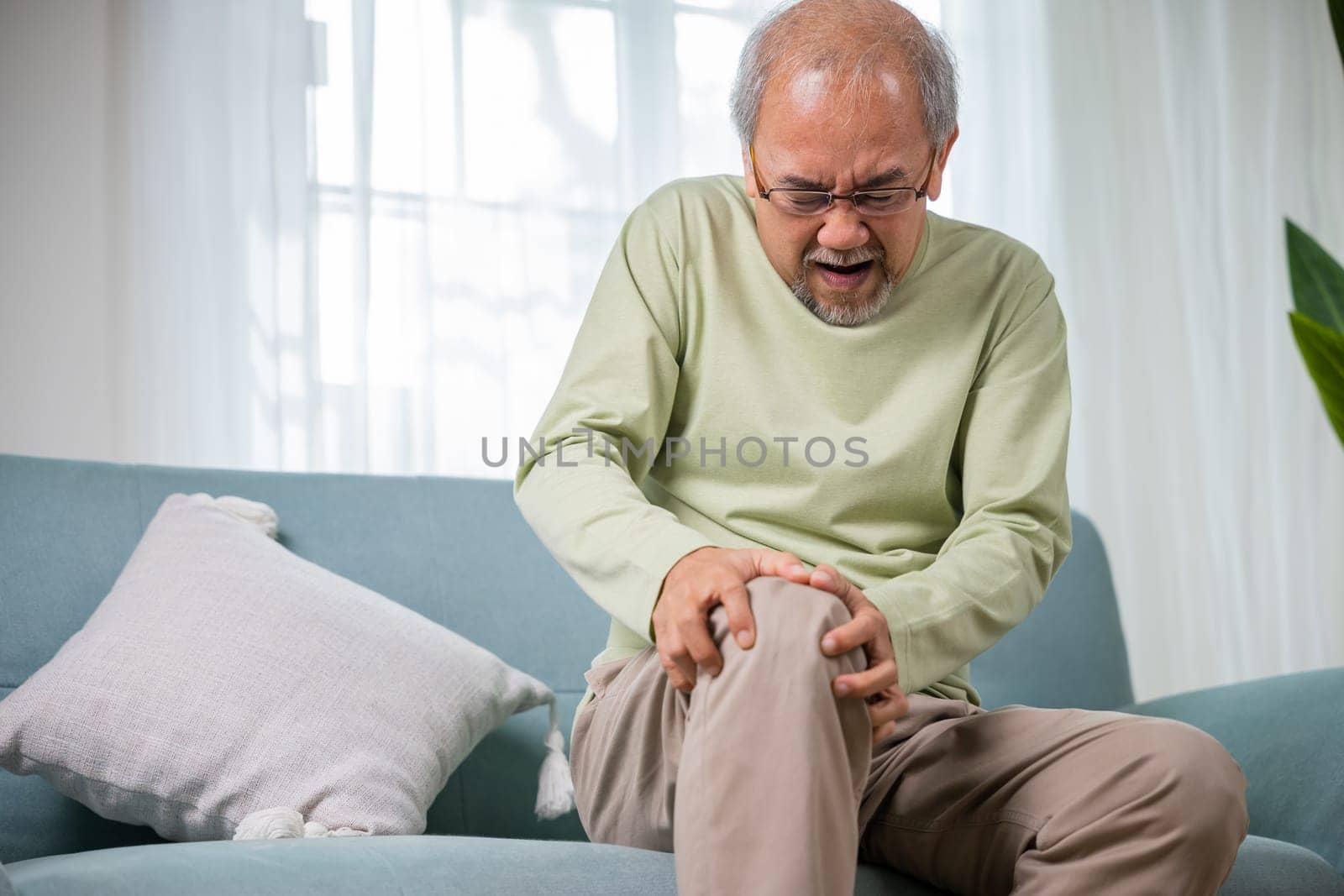 Old age. Asian senior man retirement knee joint pain on sofa, Elderly old man sitting down hands hold knee, Grandfather people health care bone problem at home