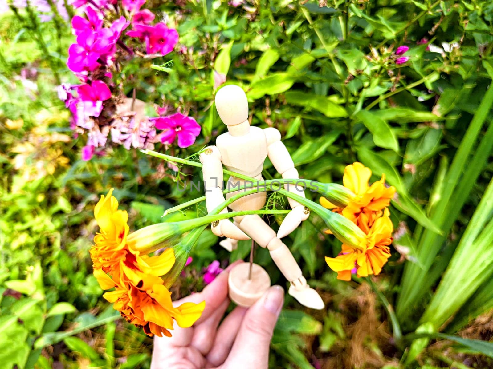 Wooden toy man with flowers in hand of woman on background grass. Concept of holiday, gift bouquet, Valentine's Day, proposal, engagement, declaration of love, Mother's Day. Caring, loving, romantic