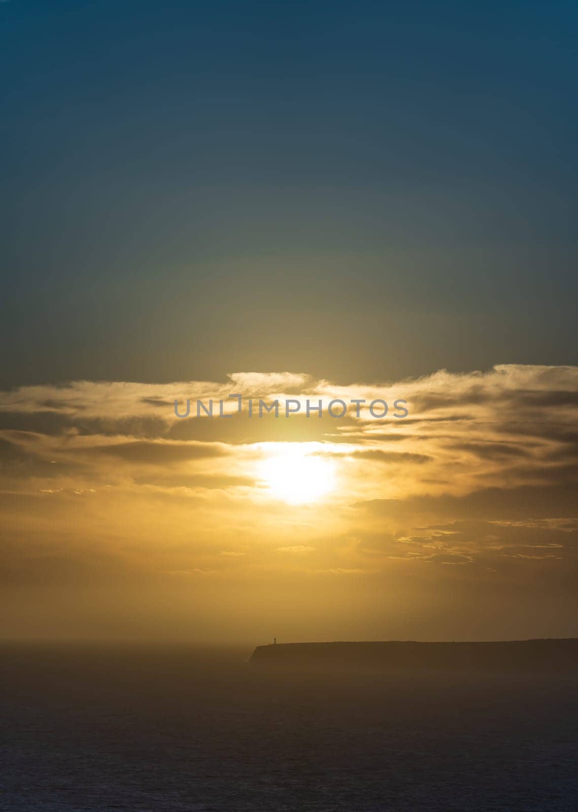 A lighthouse on cliffs creates a stunning silhouette against the sunset over the sea.