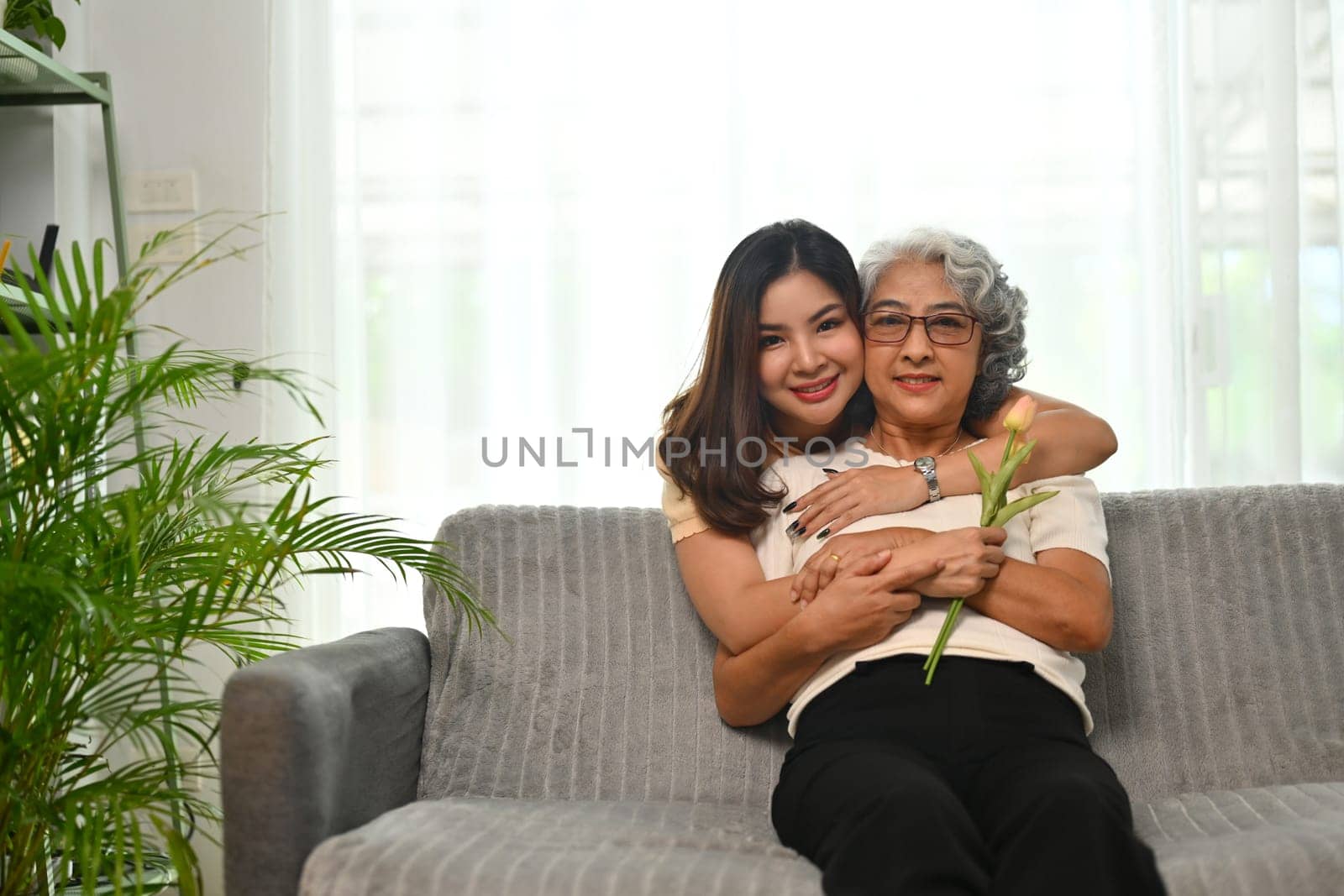 Affectionate young Asian woman hugging senior mother from back. International hug day concept.