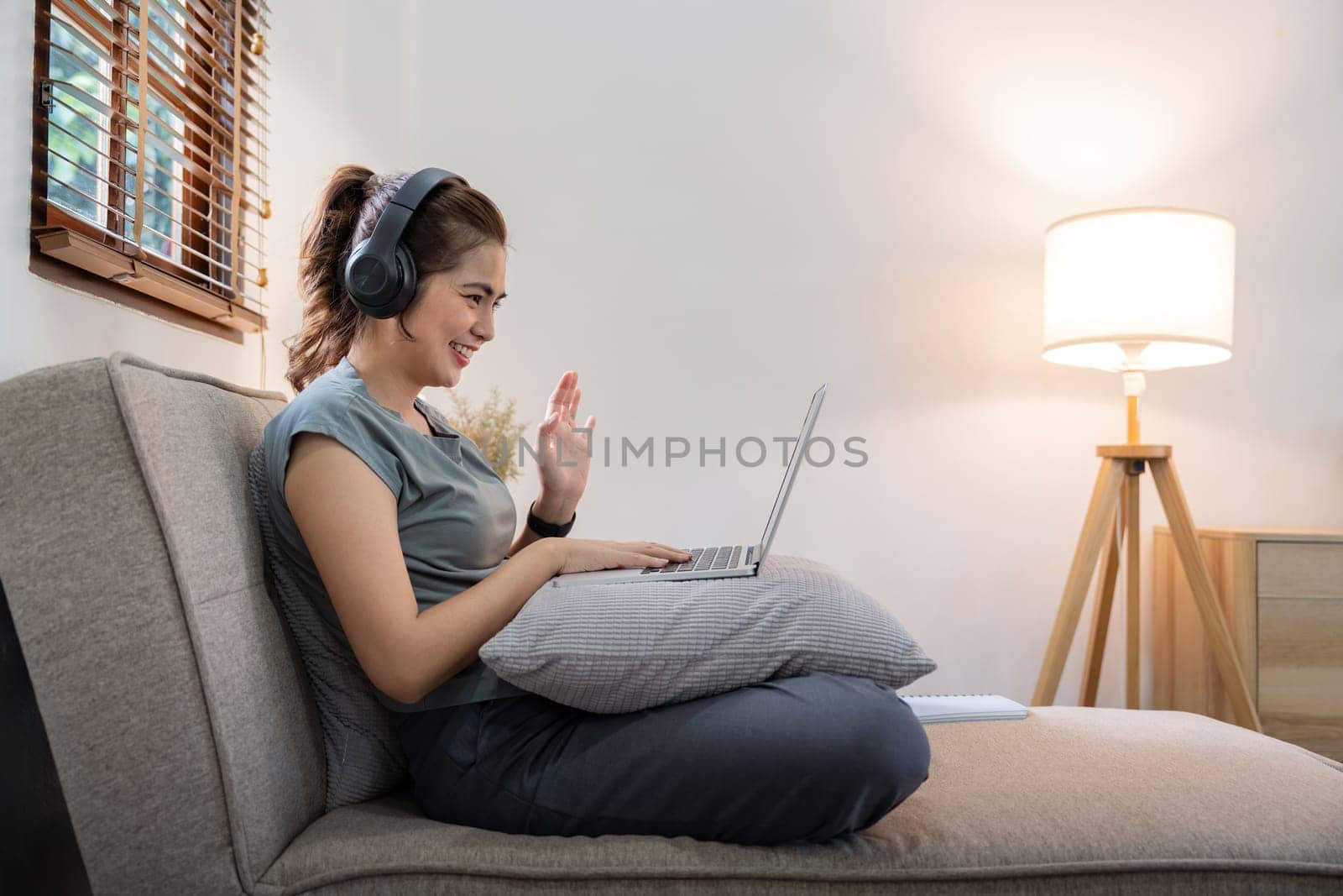 Woman asian with wear headphone video call family or friend on laptop at home by nateemee