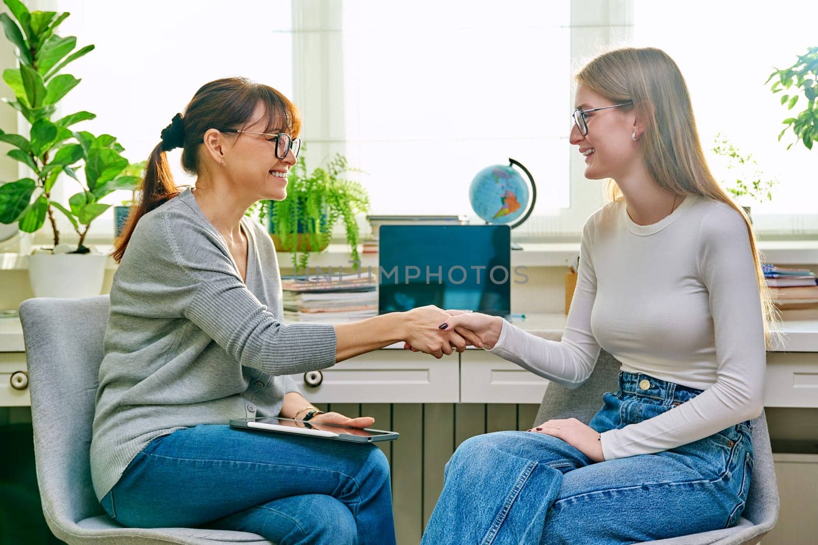 Teenager girl at mental therapy session talking to female professional counselor psychologist in therapist's office, joyful happy women shaking each other's hands successfully. Support success healing