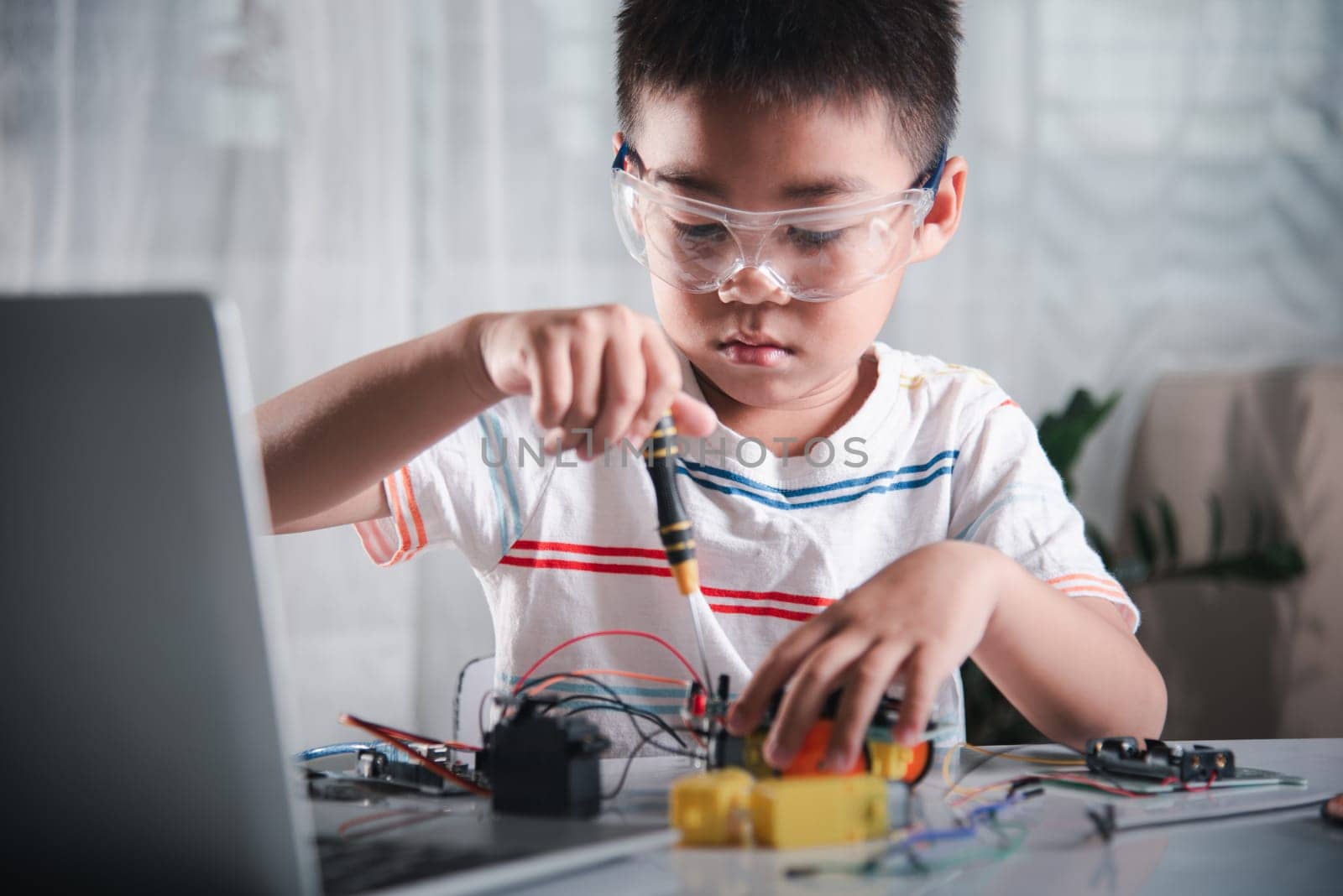 Asian kid boy assembling the Arduino robot car homework project at home by Sorapop
