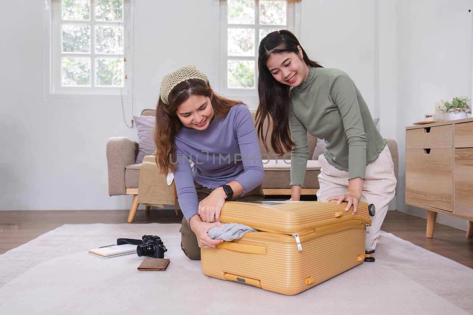Two Asian female friends pack their suitcases and plan a vacation. Before going on vacation together by wichayada
