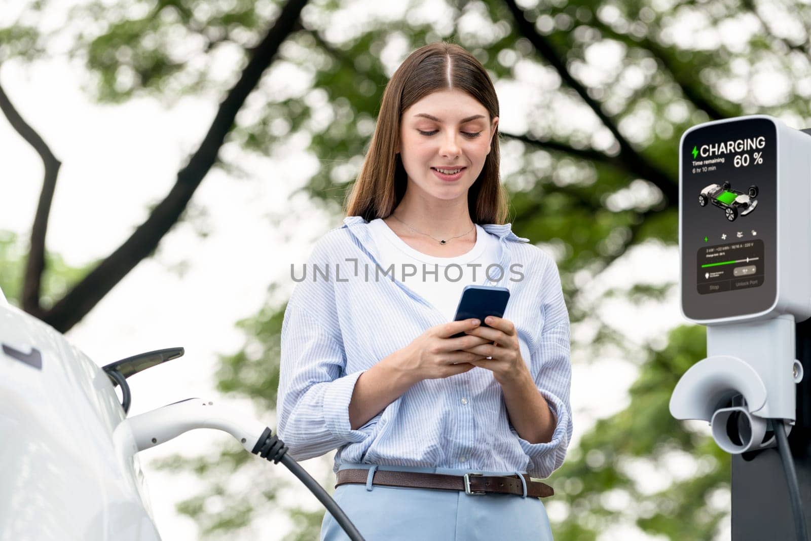 Young woman using smartphone to pay for electric car charging. Exalt by biancoblue