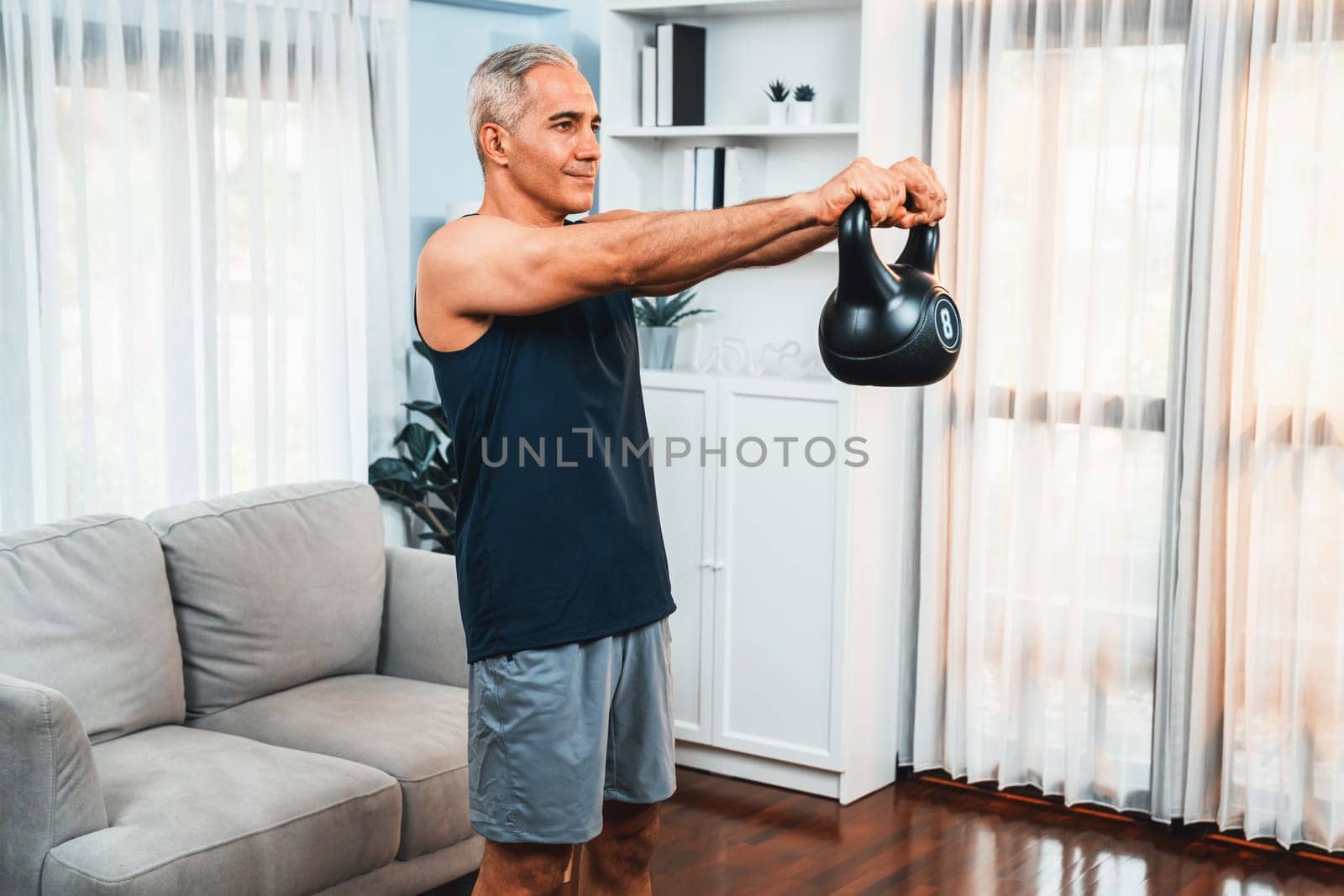 Athletic and sporty senior man lifting kettlebell at home. Clout by biancoblue