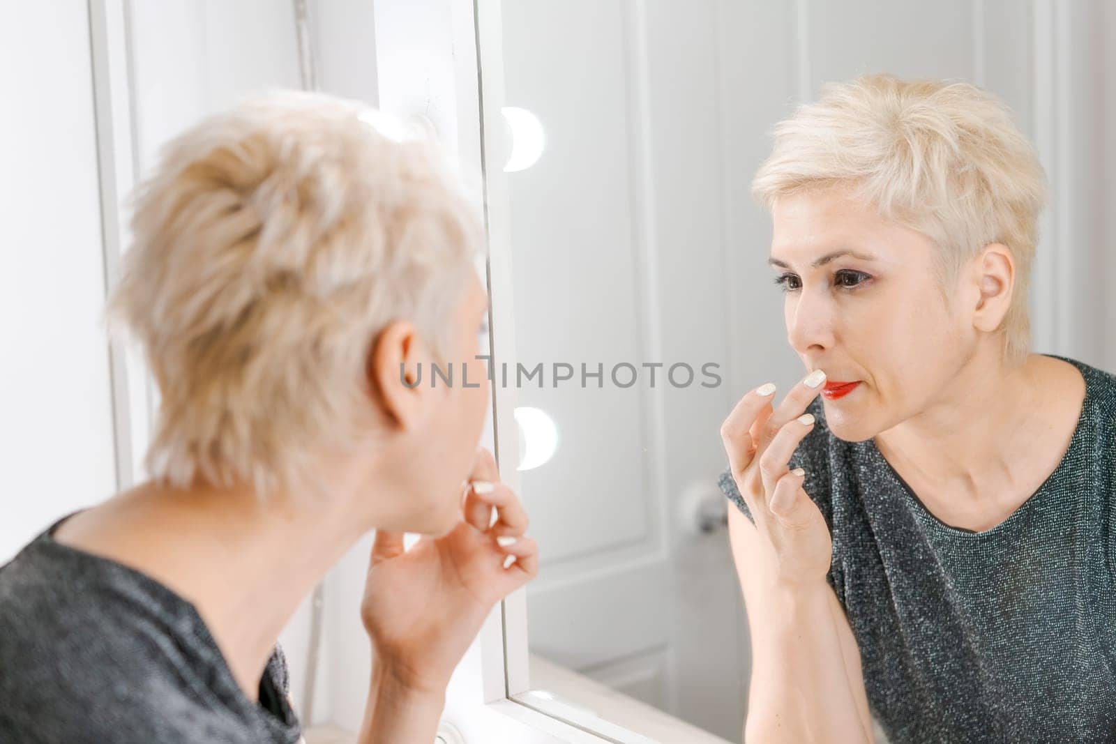 Beautiful woman with short haircut looking in mirror at her home