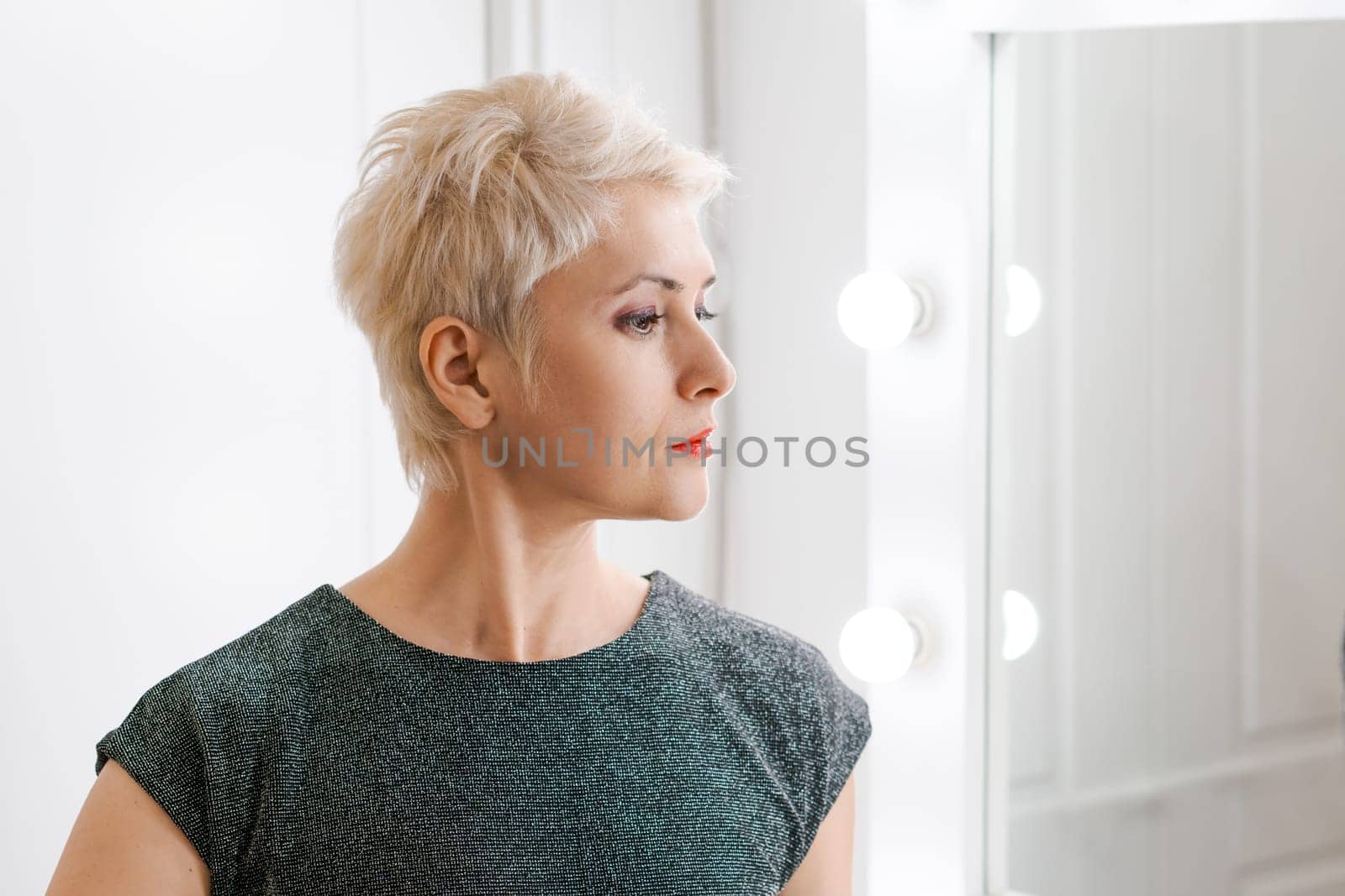 Beautiful woman with short haircut looking in mirror at her home