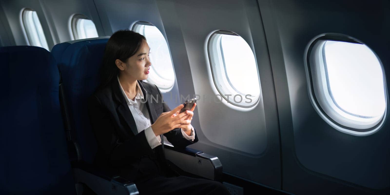 Successful Asian business woman, Business woman working in airplane on laptop computer and looking out the window along with talking on the phone.