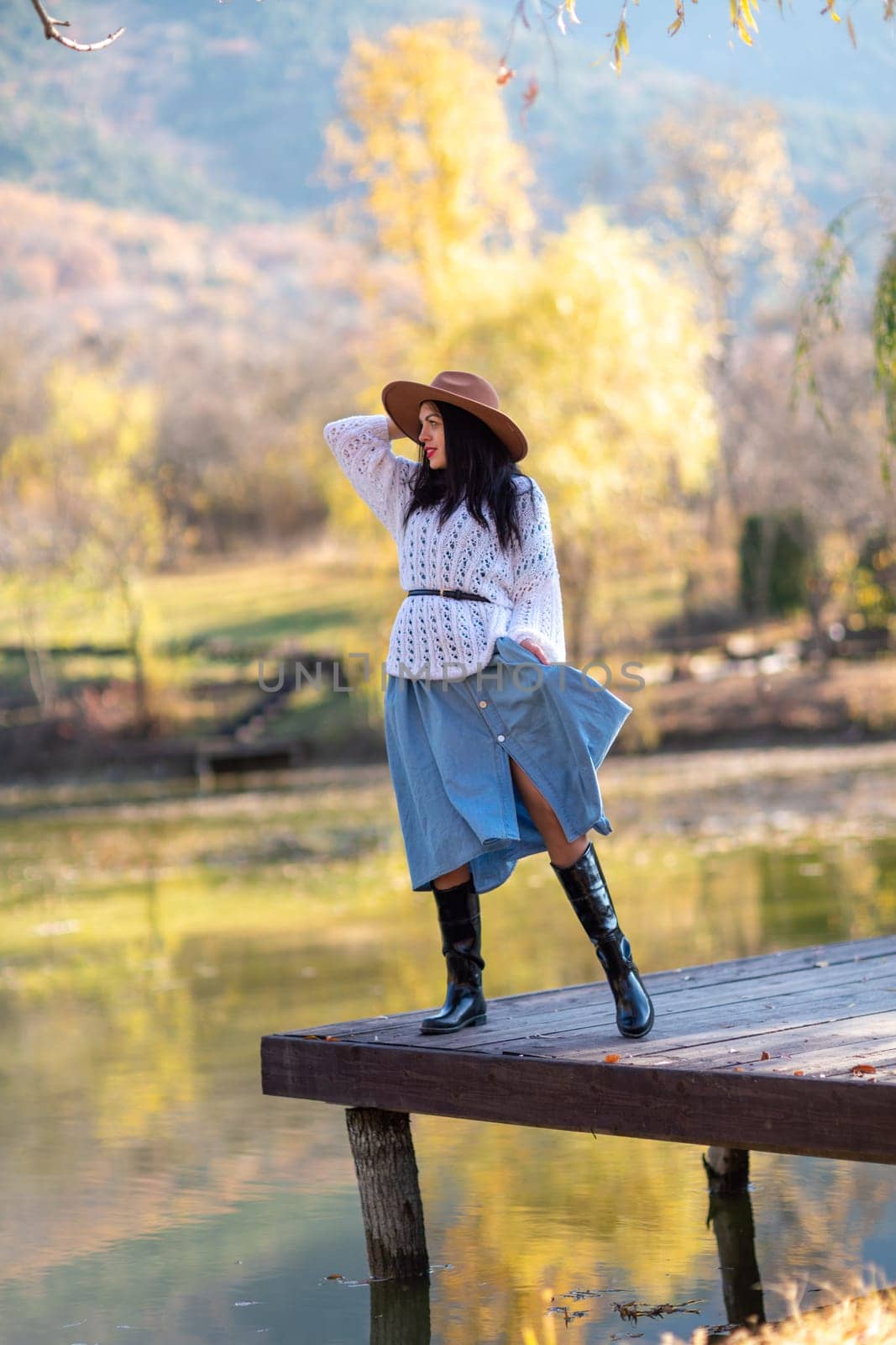 Autumn lake woman. She stands by a pond on a wooden pier in autumn and admires nature. The concept of tourism, weekends outside the city