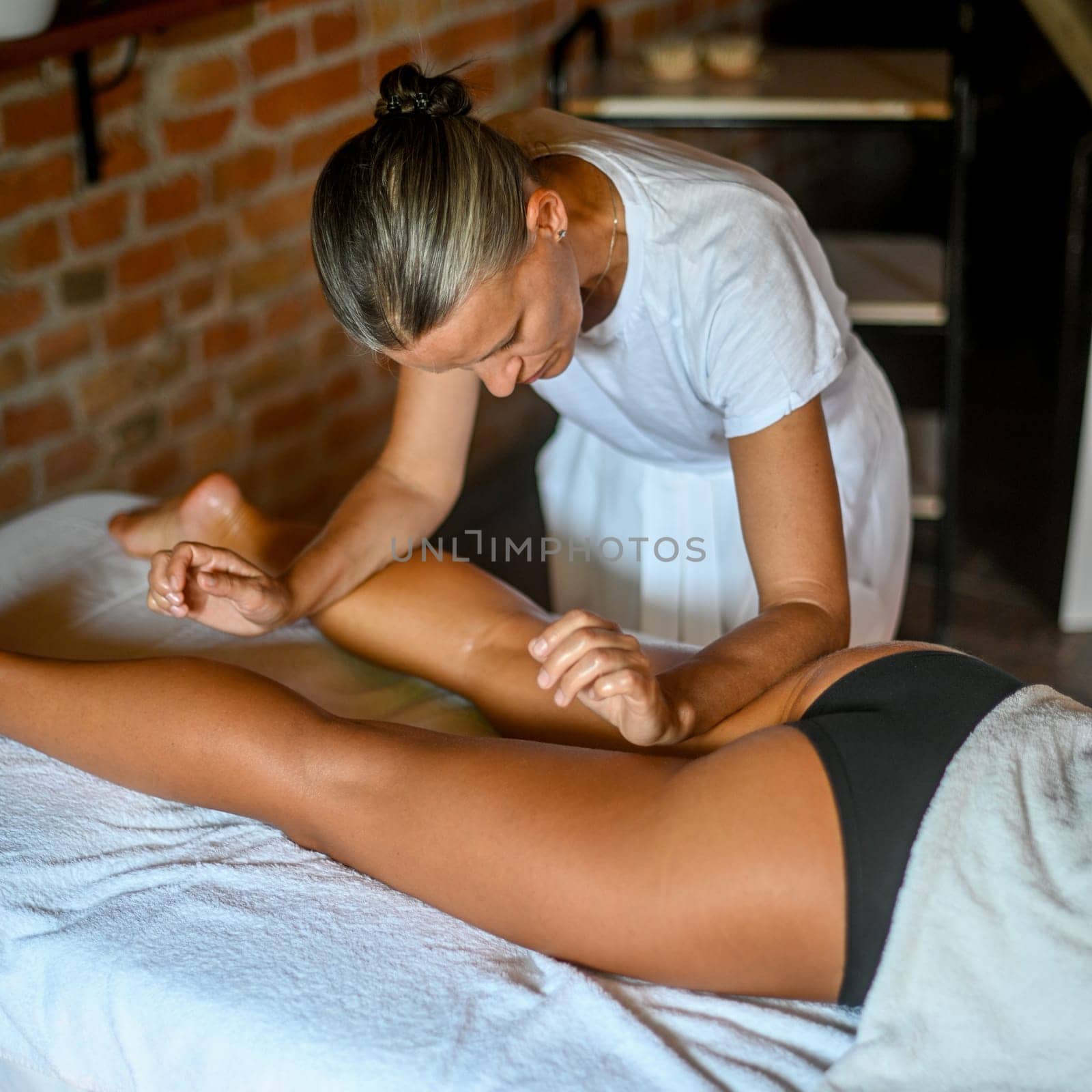 professional female physiotherapist masseuse performing leg massage to hispanic woman in spa clinic by verbano