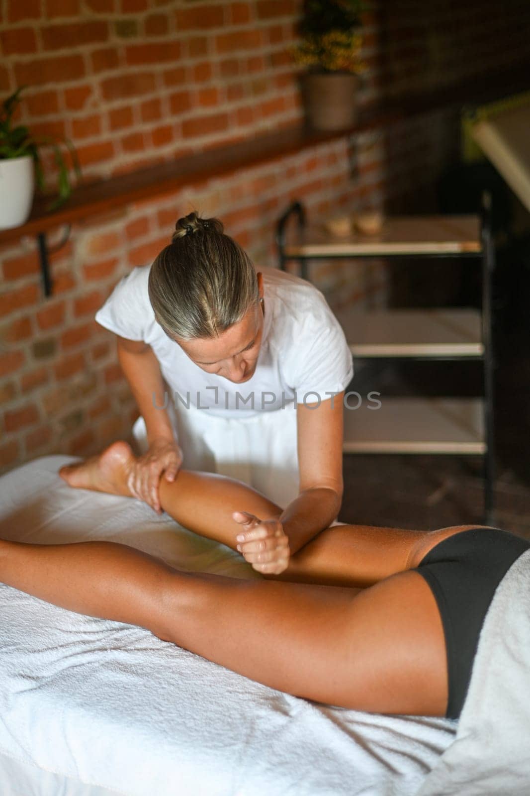 professional female physiotherapist masseuse performing leg massage to hispanic woman in spa clinic by verbano