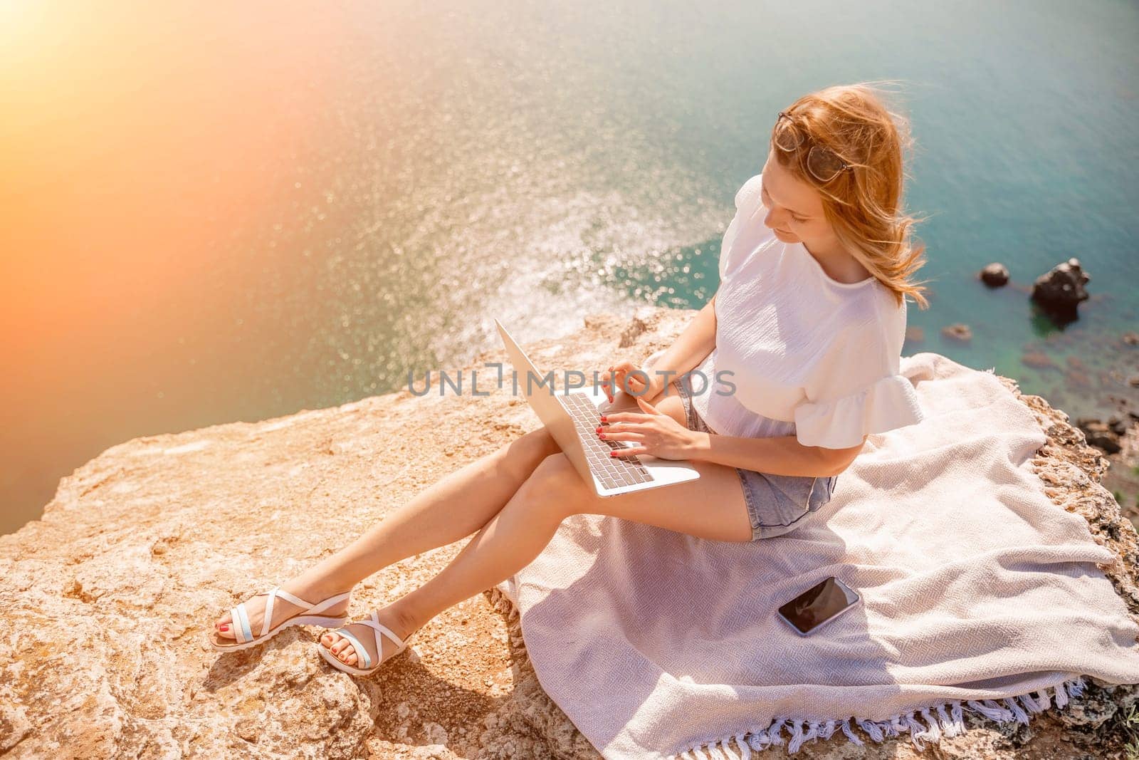 Freelance woman working on a laptop by the sea, typing away on the keyboard while enjoying the beautiful view, highlighting the idea of remote work