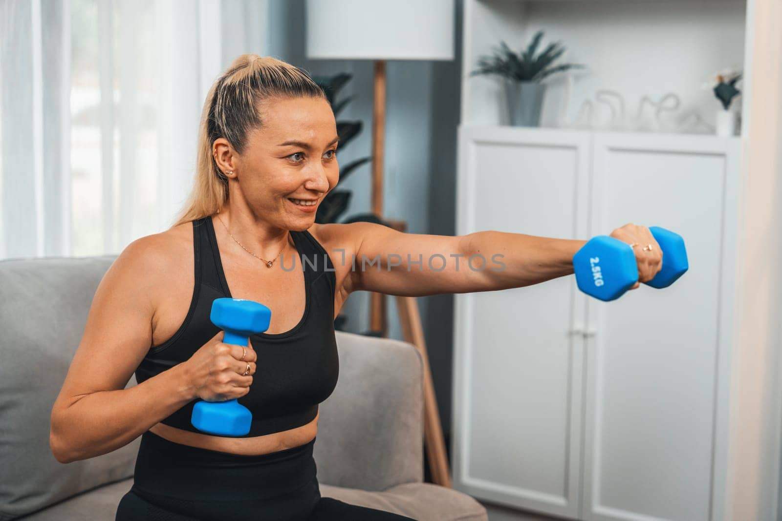 Athletic and sporty senior woman engaging in body workout routine with lifting dumbbell at home as concept of healthy fit body with body weight lifestyle after retirement. Clout