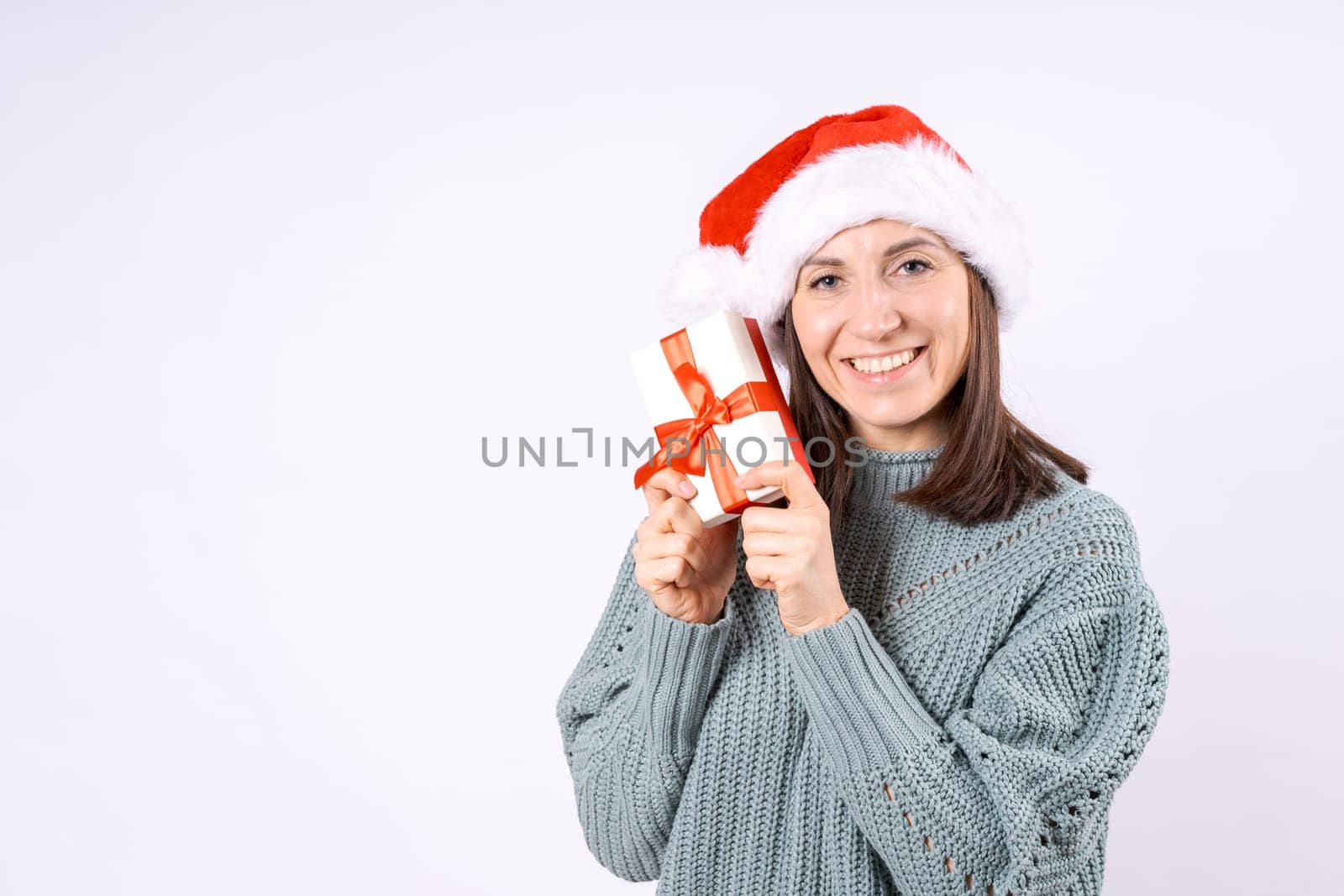 Portrait happy woman in Santa hat and sweater holding gift box on white background