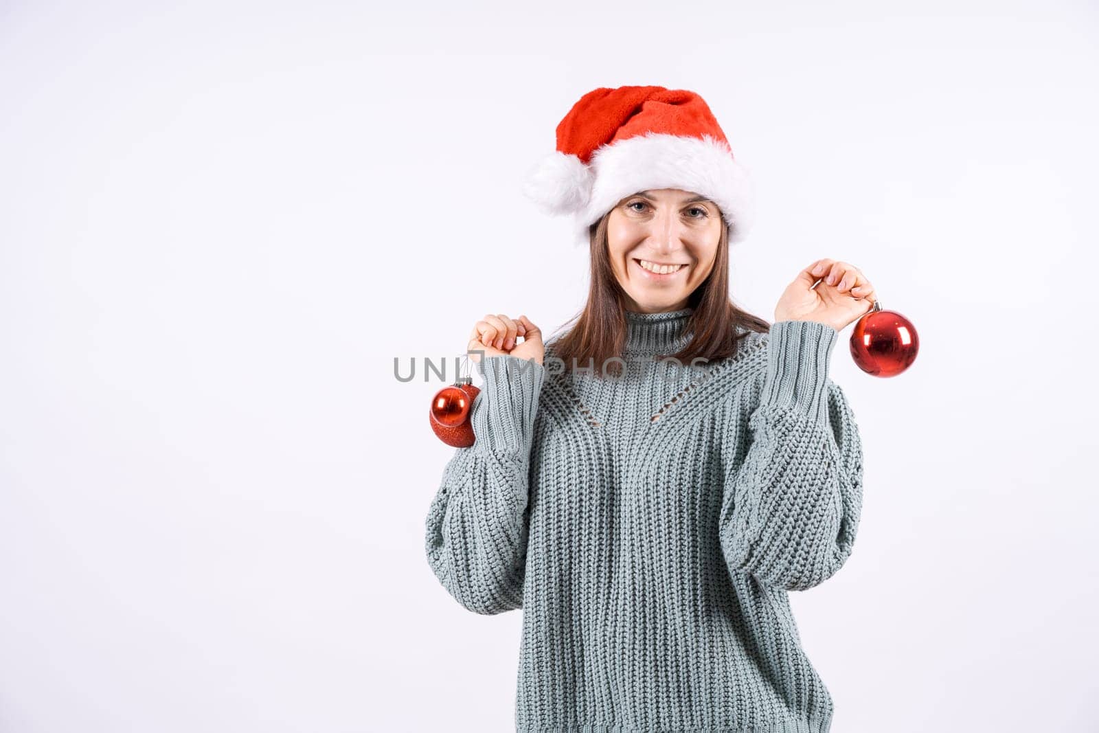 Portrait happy woman in santa hat and sweater holding red balls for Christmas tree on a white background