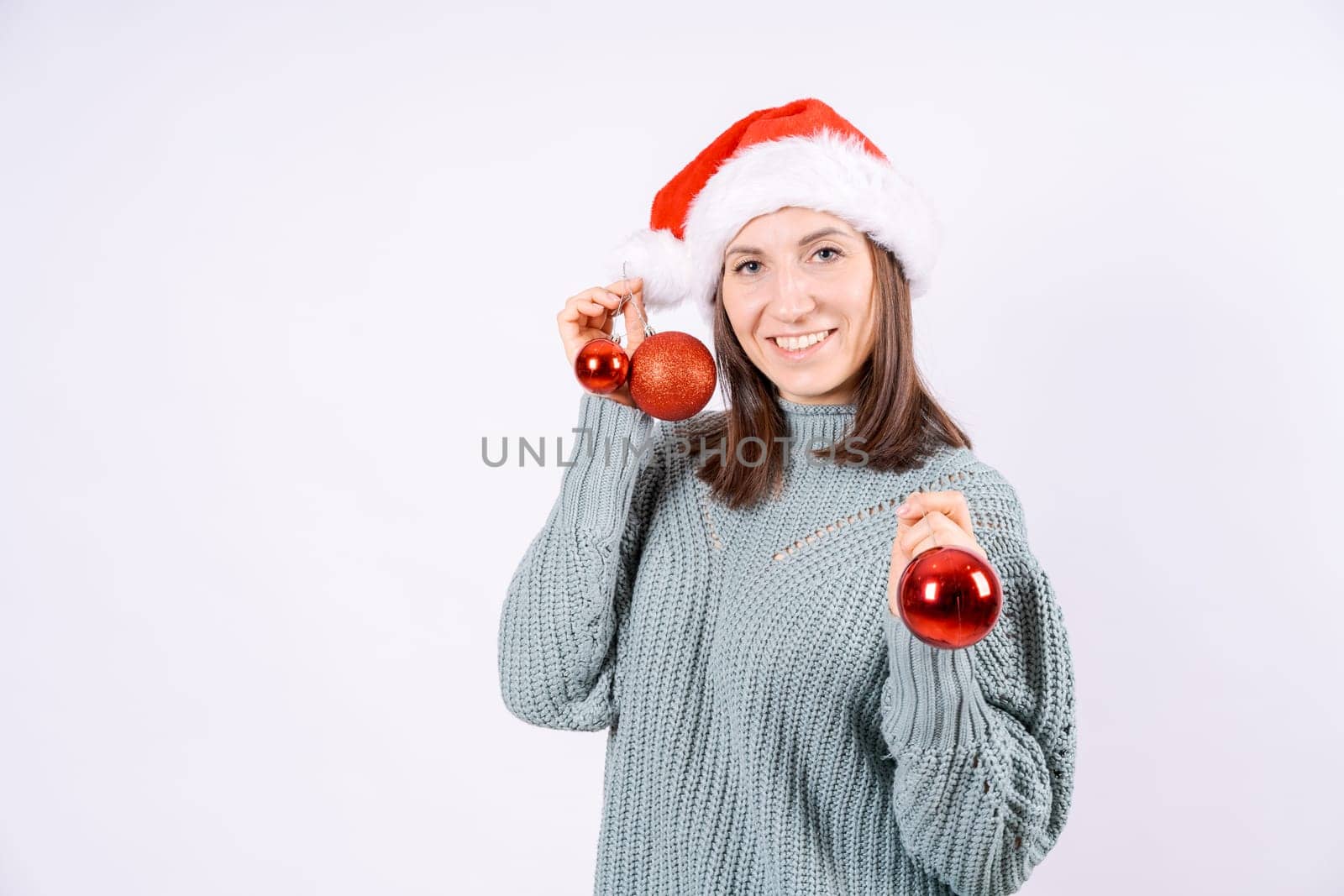 Portrait happy woman in santa hat and sweater holding red balls for Christmas tree on a white background