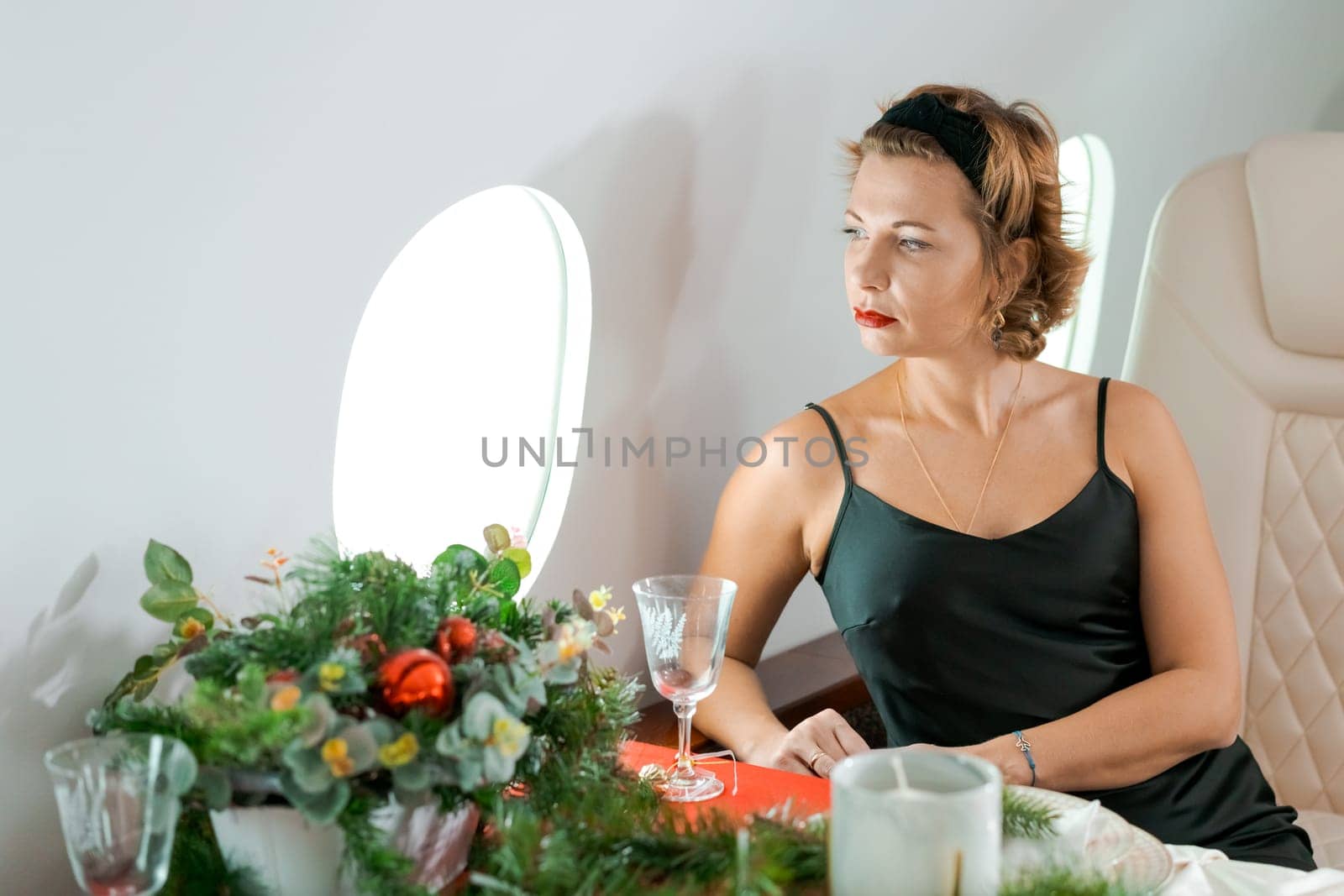 woman sits in private jet by illuminator, decorated for Christmas, New Year's Eve flight, holiday and travel concept