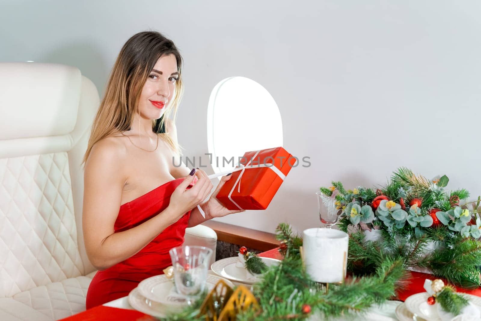 woman sits in private jet by illuminator, decorated for Christmas, New Year's Eve flight, holiday and travel concept