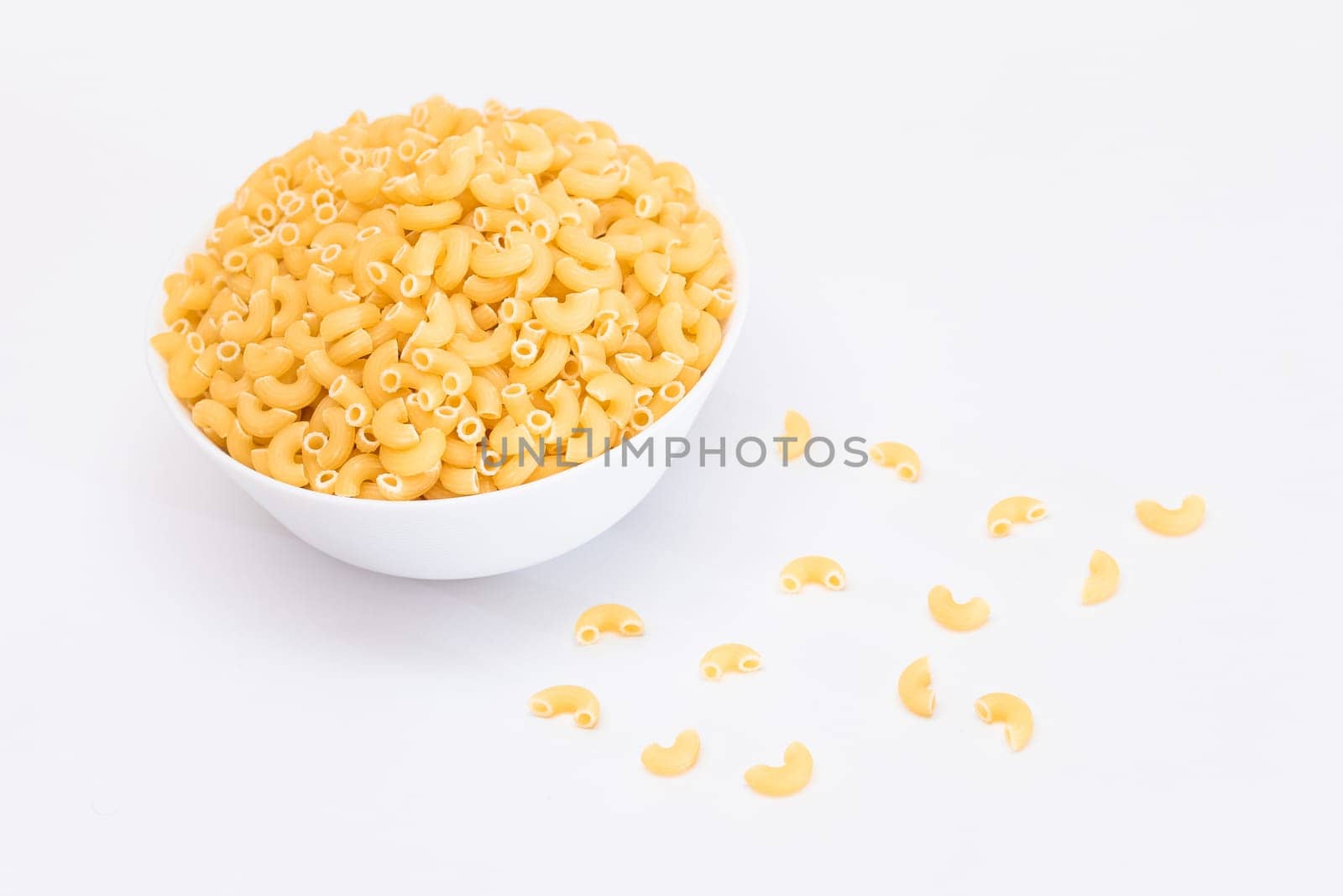 Uncooked Chifferi Rigati Pasta in White Cup Isolated on White Background. Fat and Unhealthy Food. Scattered Classic Dry Macaroni. Italian Culture and Cuisine. Raw Pasta - Isolation
