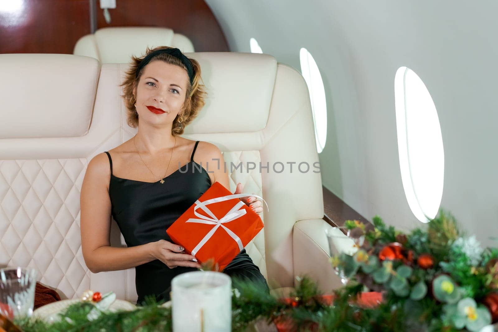 Woman sitting in private plane holding box with gift, for Christmas, New Year's Eve flight, holiday and travel concept. by EkaterinaPereslavtseva