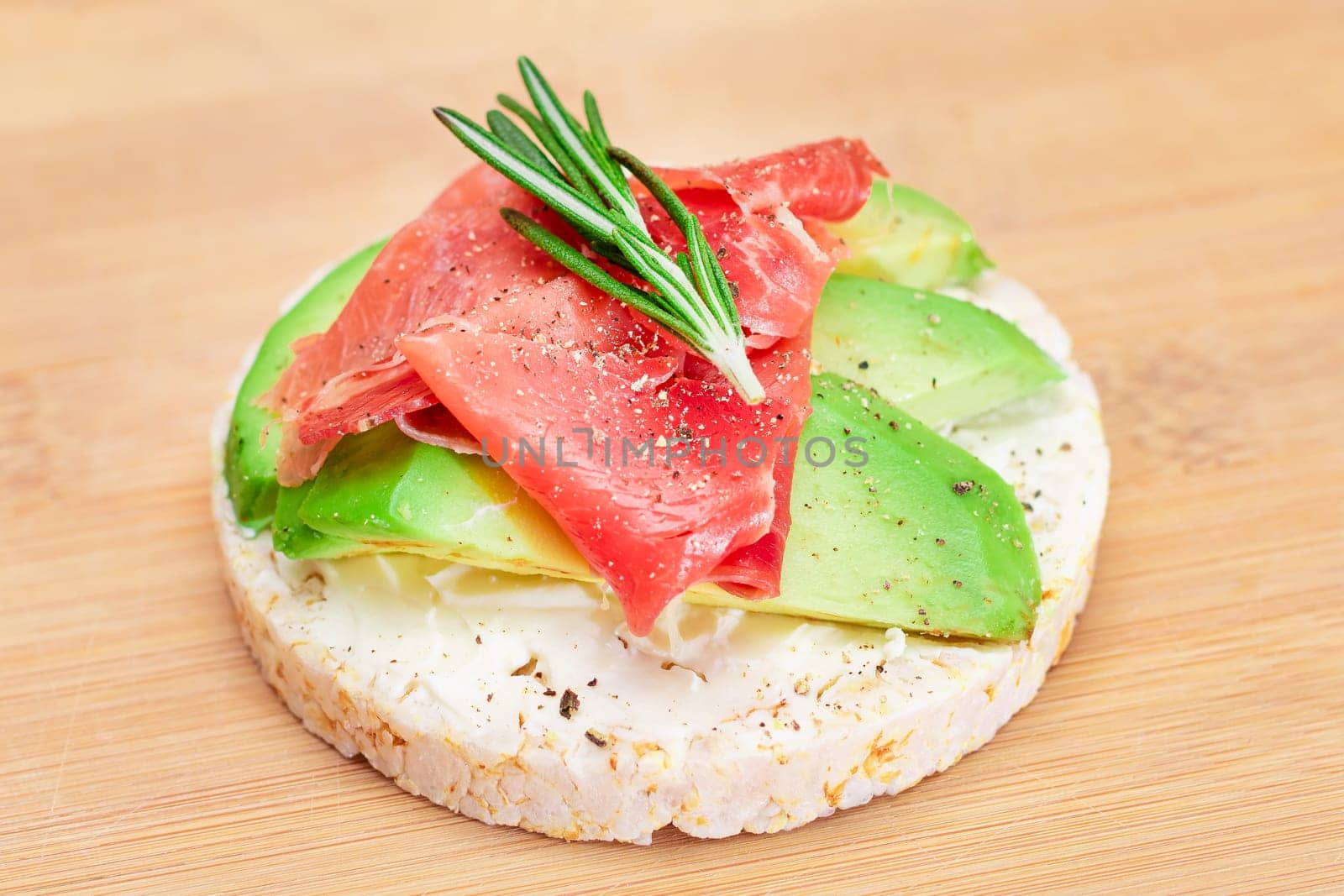 Rice Cake Sandwich with Fresh Avocado, Jamon and Rosemary on Bamboo Cutting Board. Easy Breakfast. Diet Food. Quick and Healthy Sandwiches. Crispbread with Tasty Filling. Healthy Dietary Snack