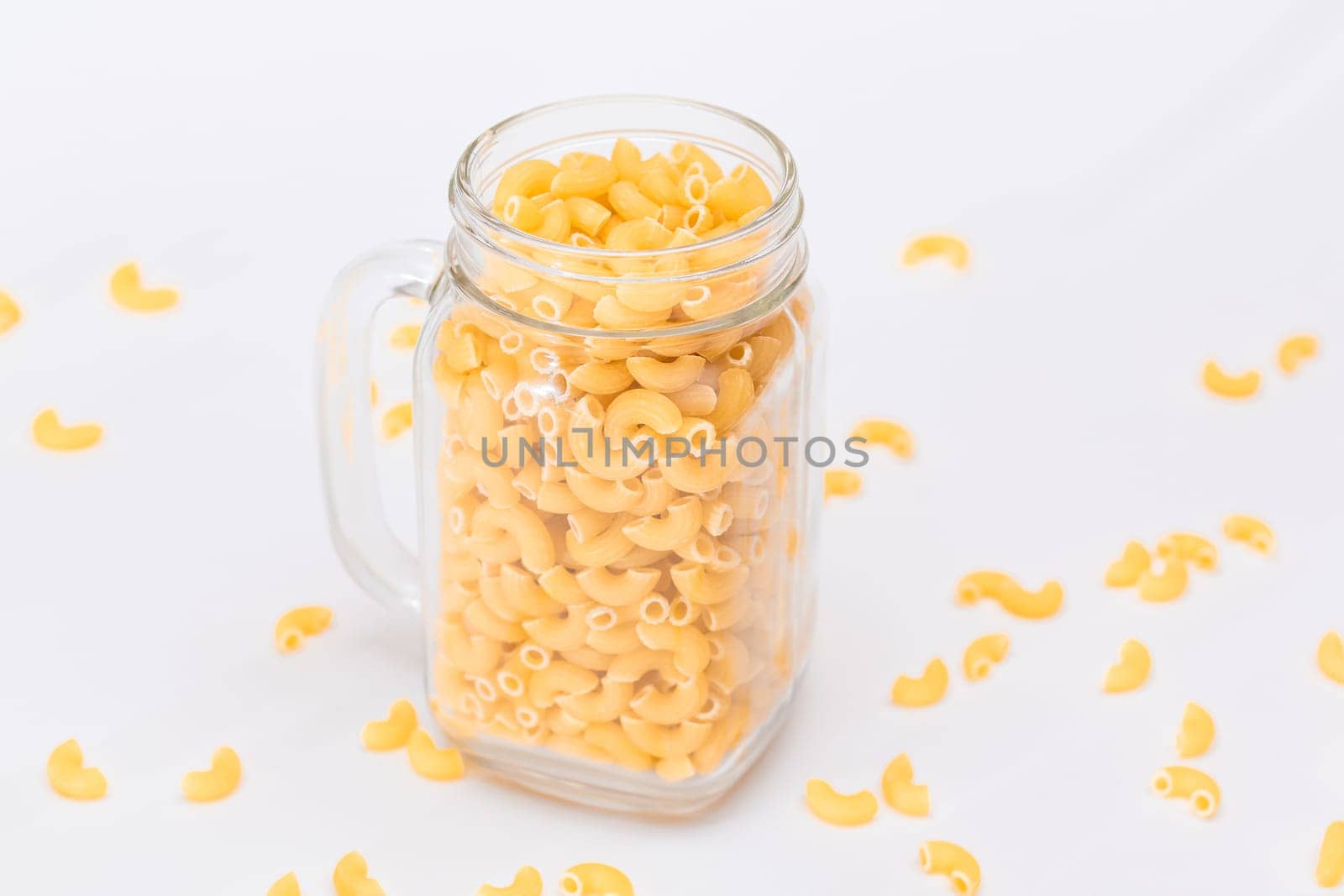 Uncooked Chifferi Rigati Pasta in Glass Jar on White Background. Fat and Unhealthy Food. Scattered Classic Dry Macaroni. Italian Culture and Cuisine. Raw Pasta