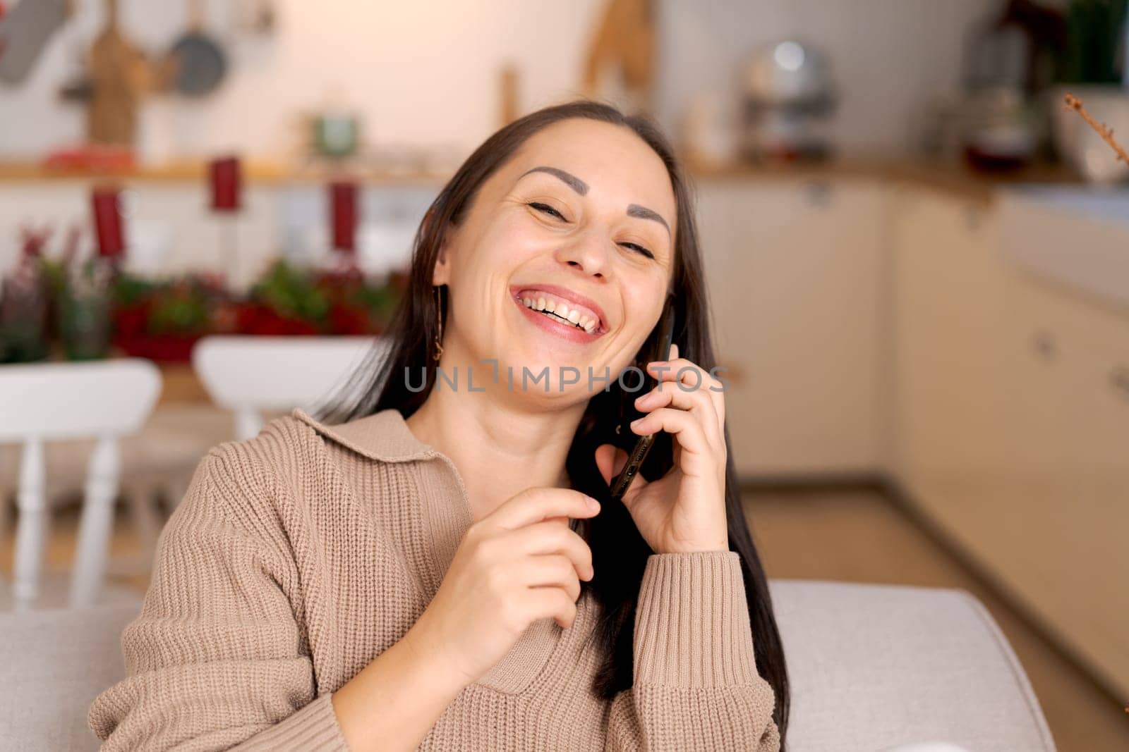 Woman with phone in hands sitting at home in kitchen on sofa during christmas holidays