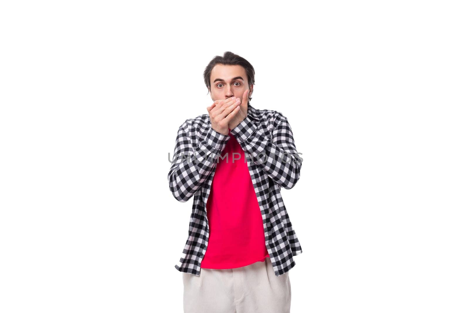 young surprised european brutal guy with chic hair and beard covered his mouth with his hand on a white background with copy space.