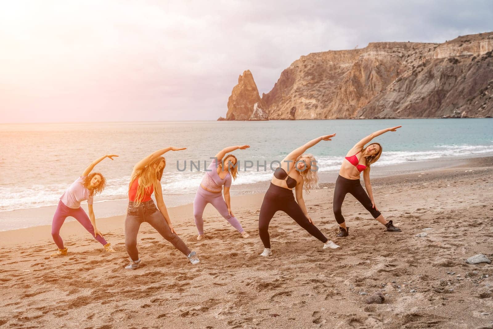A group of five female friends are doing exercises on the beach. Beach holiday concept, healthy lifestyle.