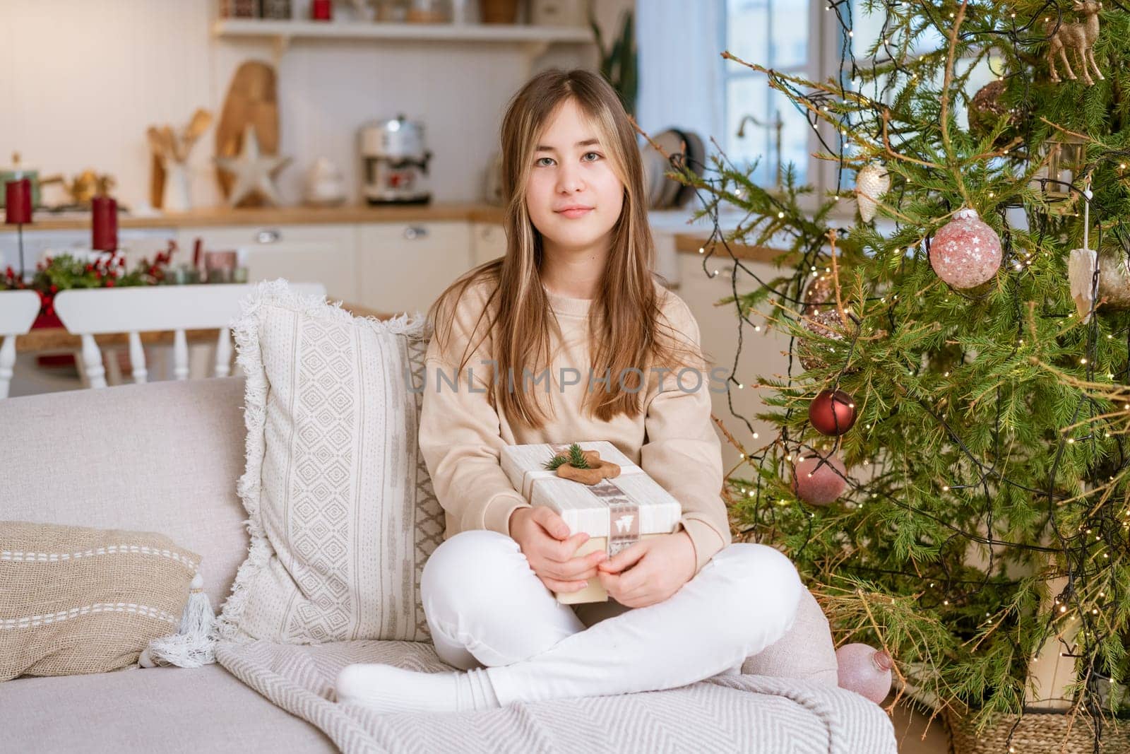 A cute girl sits on the couch with a Christmas present from her family. by EkaterinaPereslavtseva