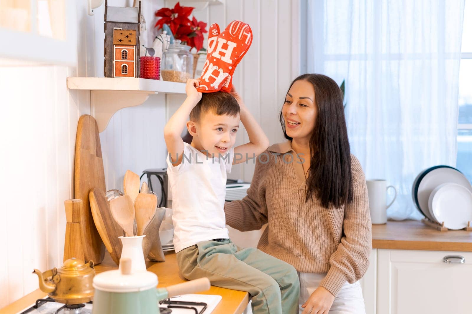 Fun mom and son playing in kitchen, happy spending time on Christmas Eve by EkaterinaPereslavtseva