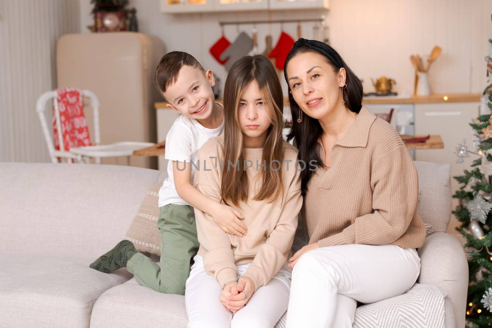 Family in decorated house on Christmas Day sitting on couch. Mother and son hug sad daughter. Selective focus